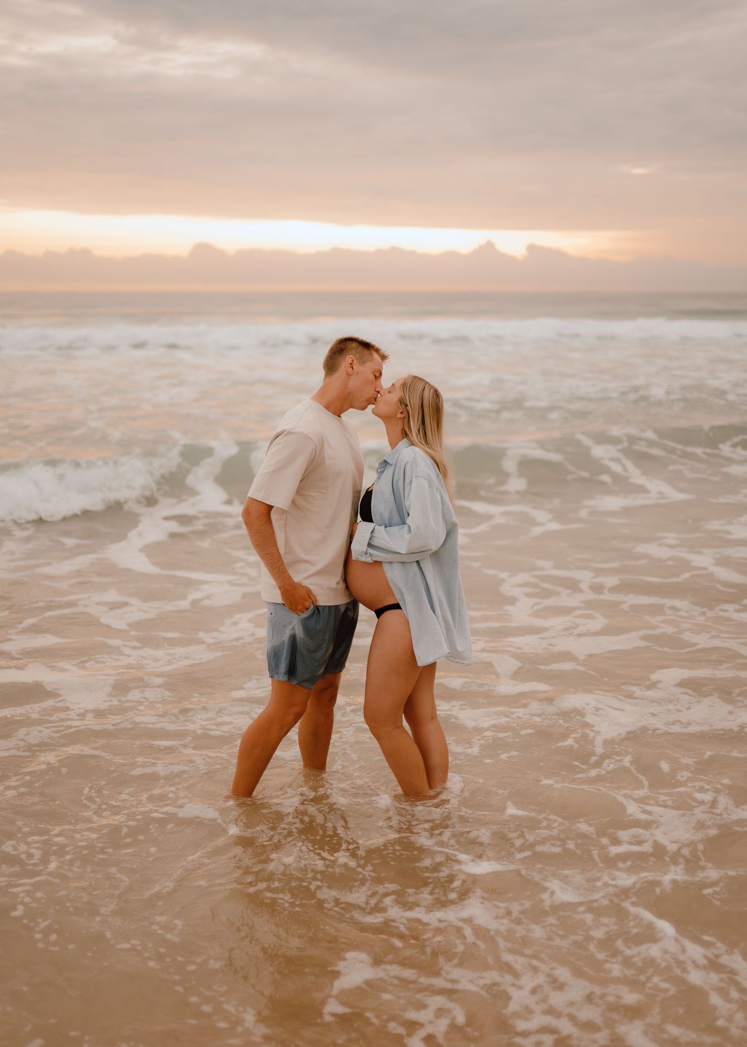 A couple shares romantic moments in the ocean waves during sunset, creating a dreamy beach photoshoot sequence.