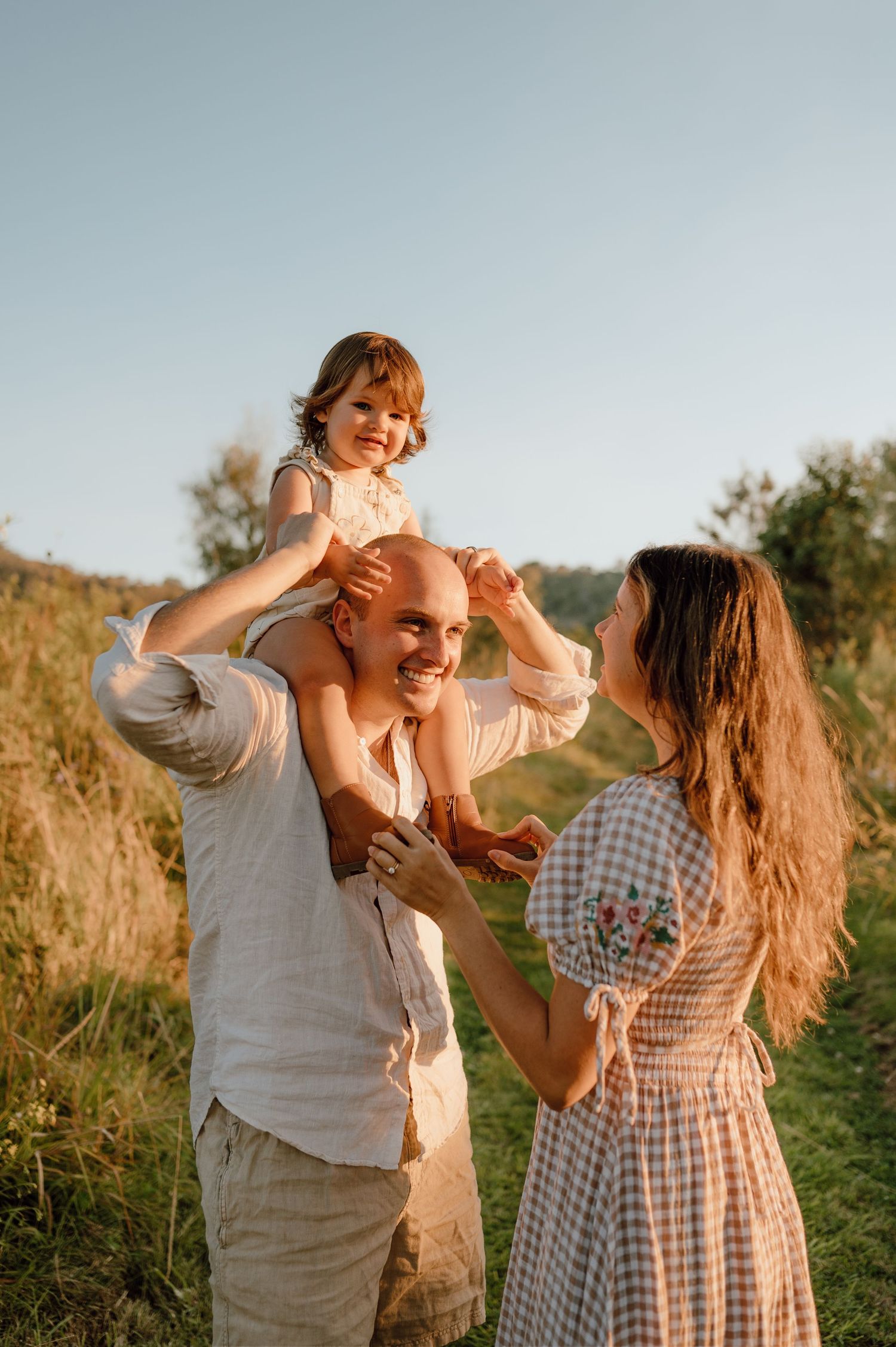 Family shares joyful laughter together in a grassy field at sunset.