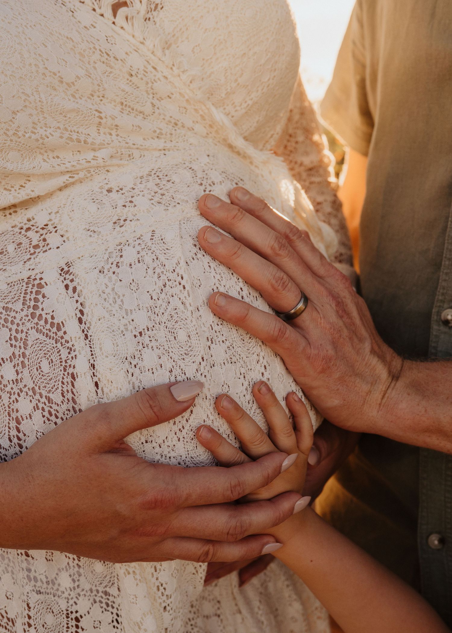 Close-up sequence of hands with wedding rings touching and intertwining against white lace in warm sunlight.