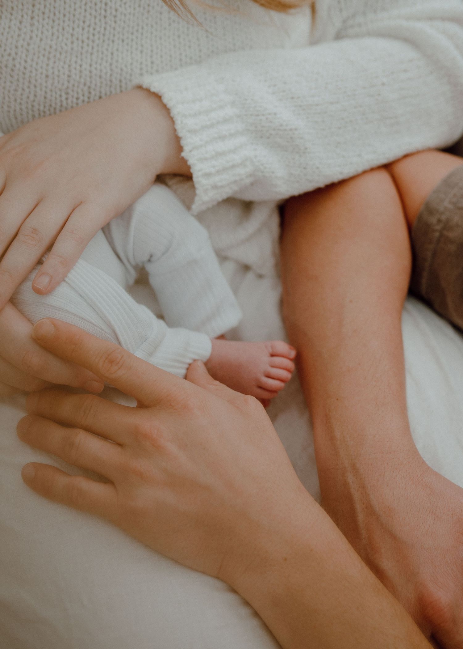 Close-up of gentle hands holding tiny baby feet wearing white socks against soft fabric background.