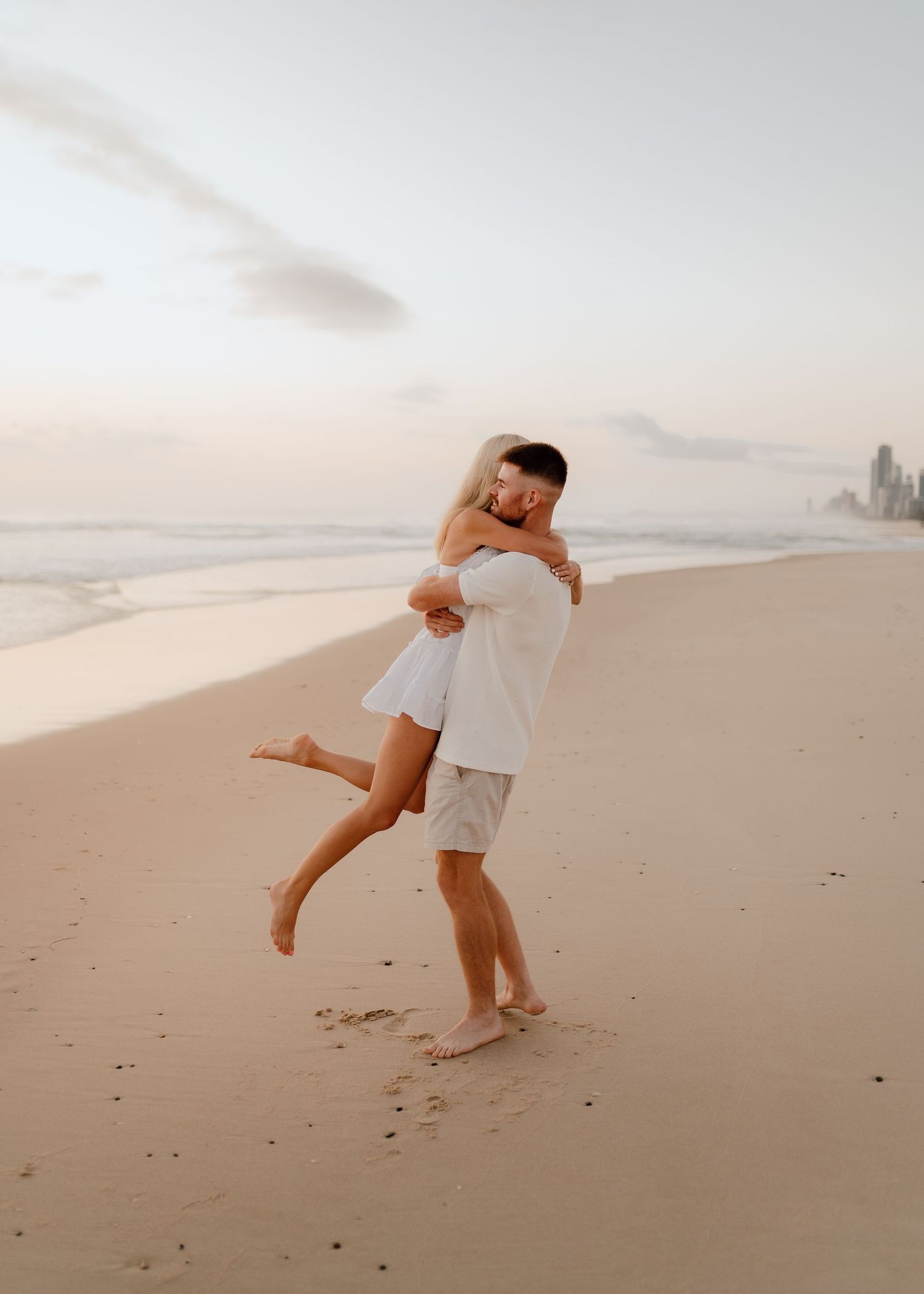 A couple shares a romantic moment dancing together on a sandy beach at sunset.