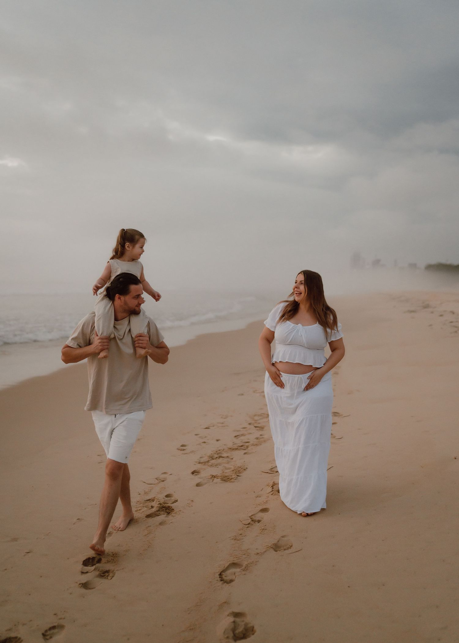 Two people playfully chase each other along a misty beach shoreline leaving footprints in the sand at sunset.
