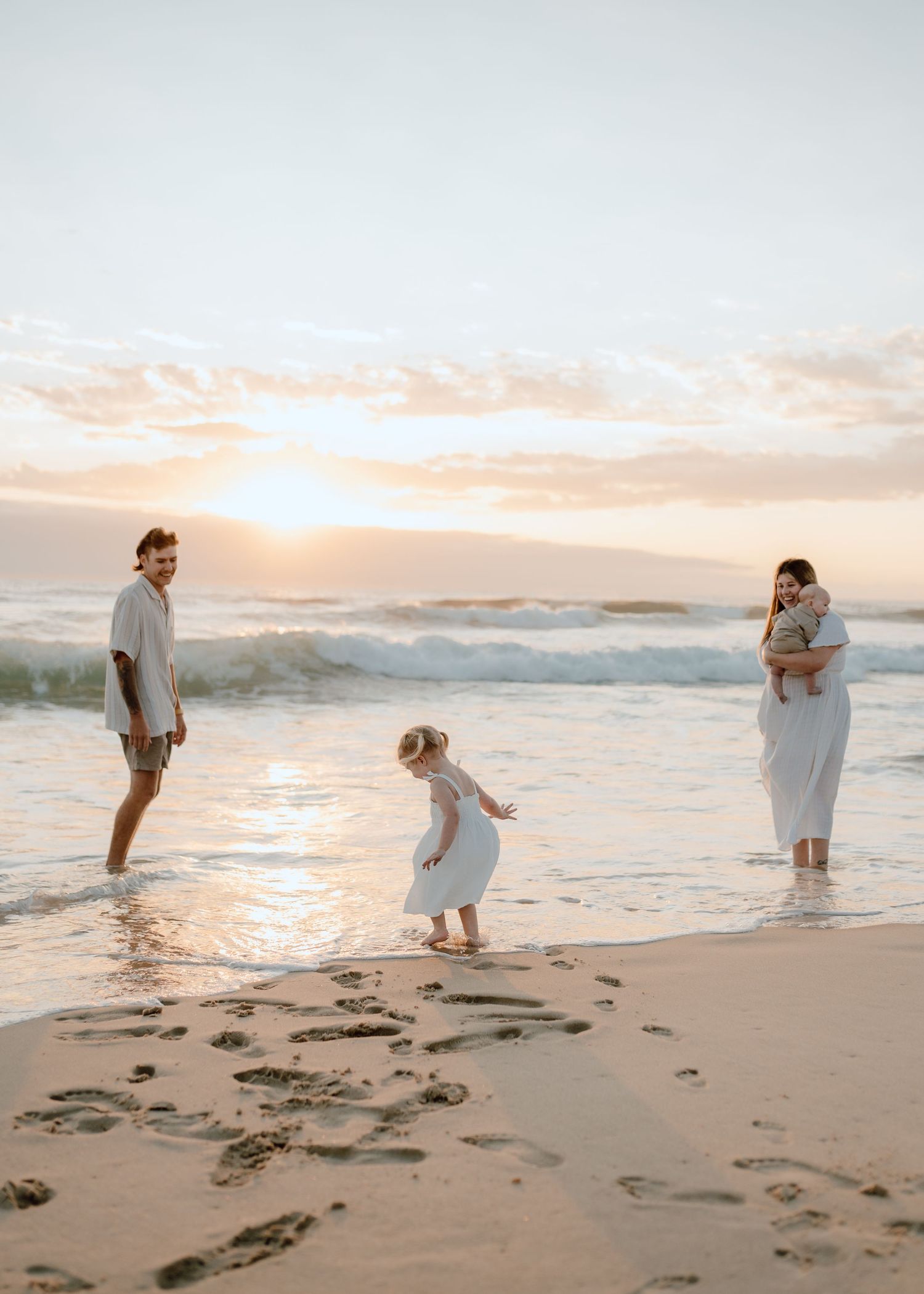 Family walking and playing together on beach with sunset ocean waves in background.