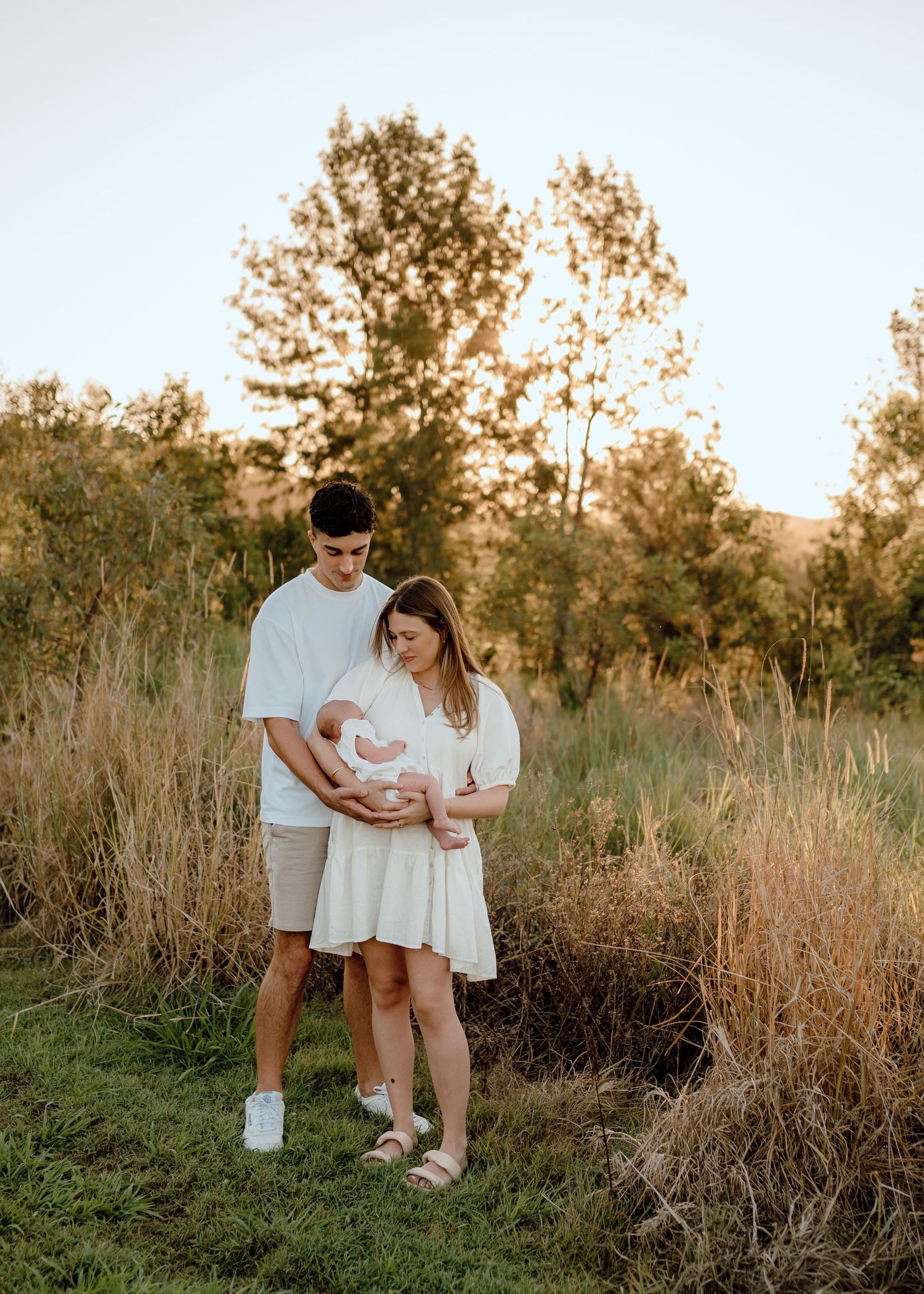 Family of three enjoying a sunset photoshoot in a natural outdoor setting with tall grass.