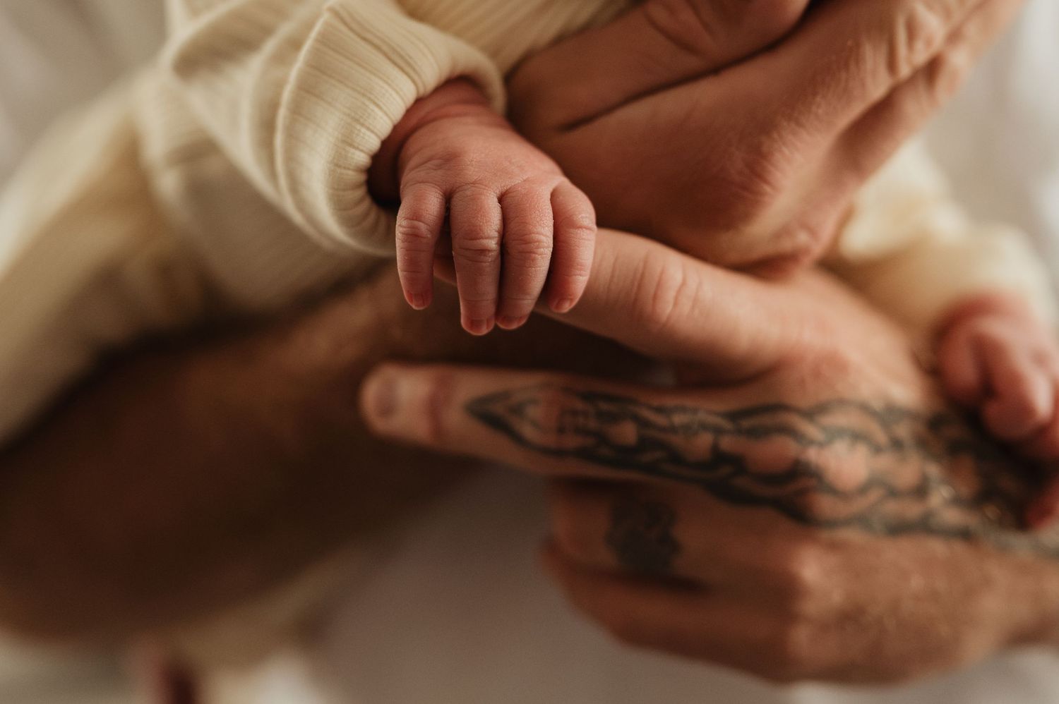 Close-up of a newborn baby's tiny hand resting on a tattooed adult's finger, symbolizing new life and parental love.