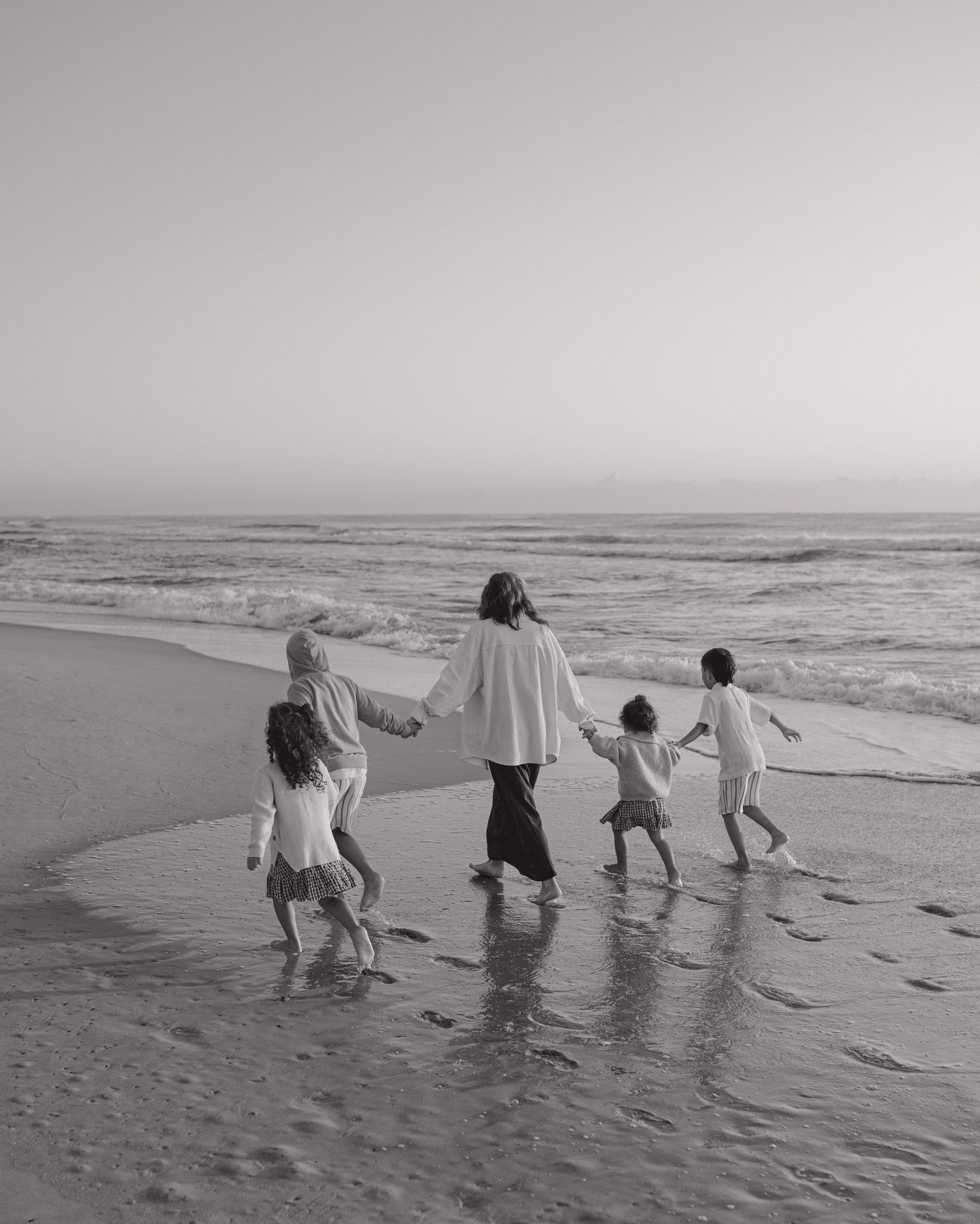 Black and white photo of group walking through ocean waves on beach.