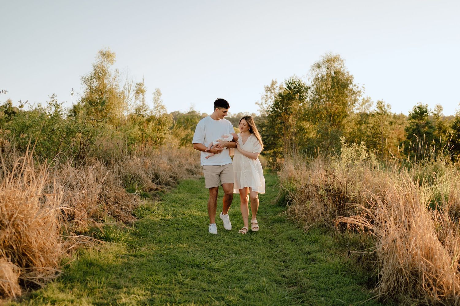 Family walking together on a grassy path during golden hour with tall grass and trees in background.