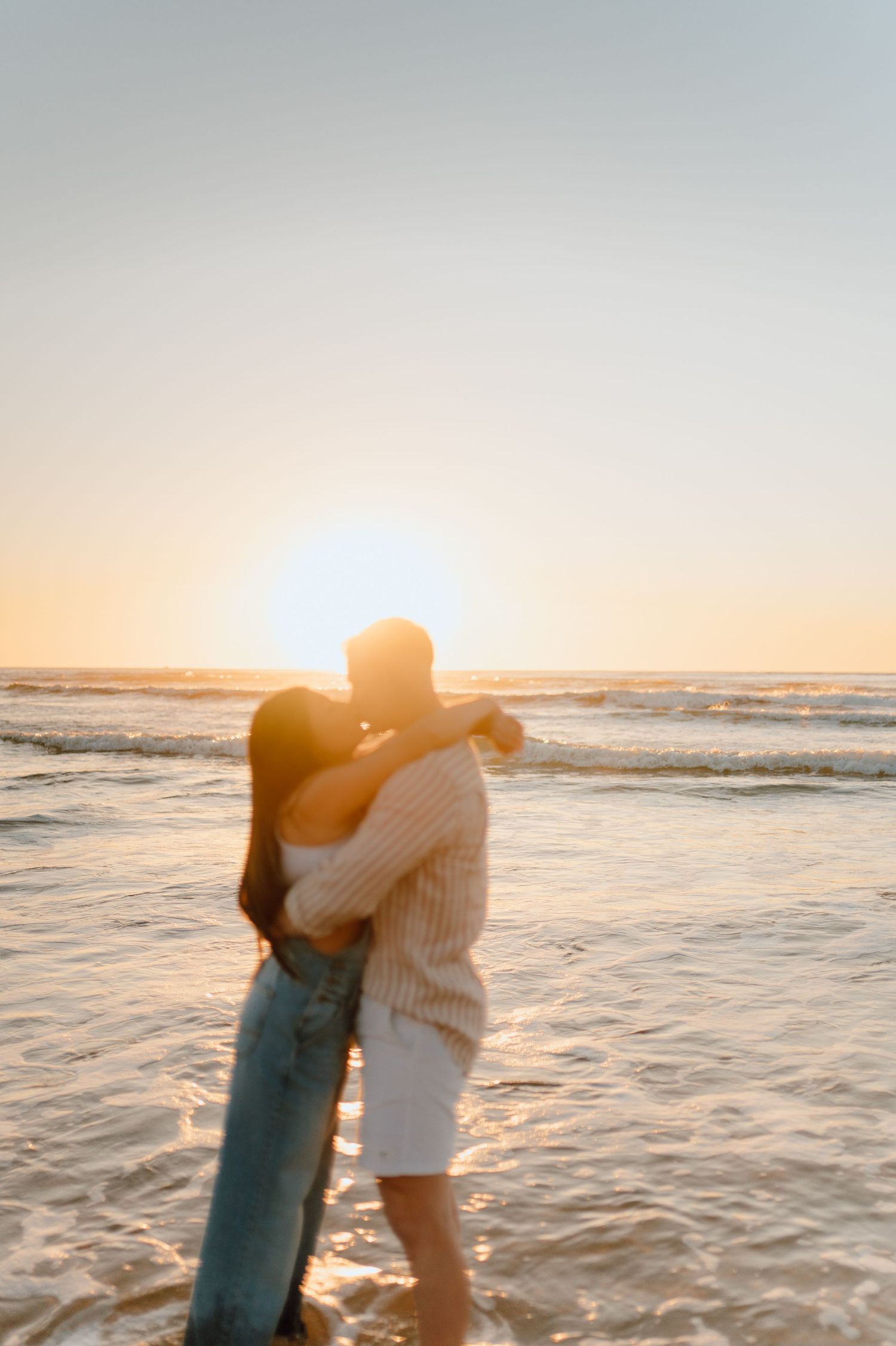A couple shares a romantic moment in the ocean waves during sunset.
