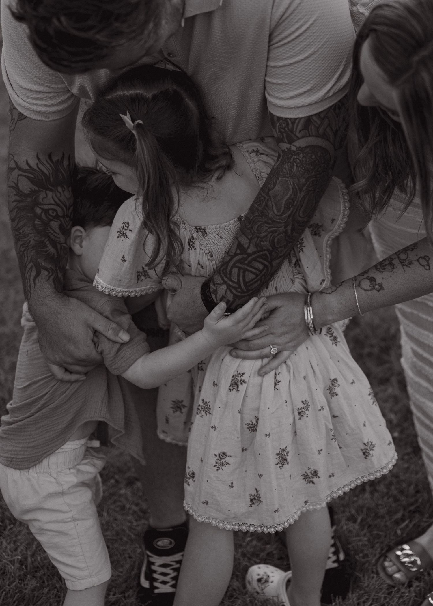 Black and white photo showing children in summer outfits gathered together, with visible tattoo art on an adult's arm.