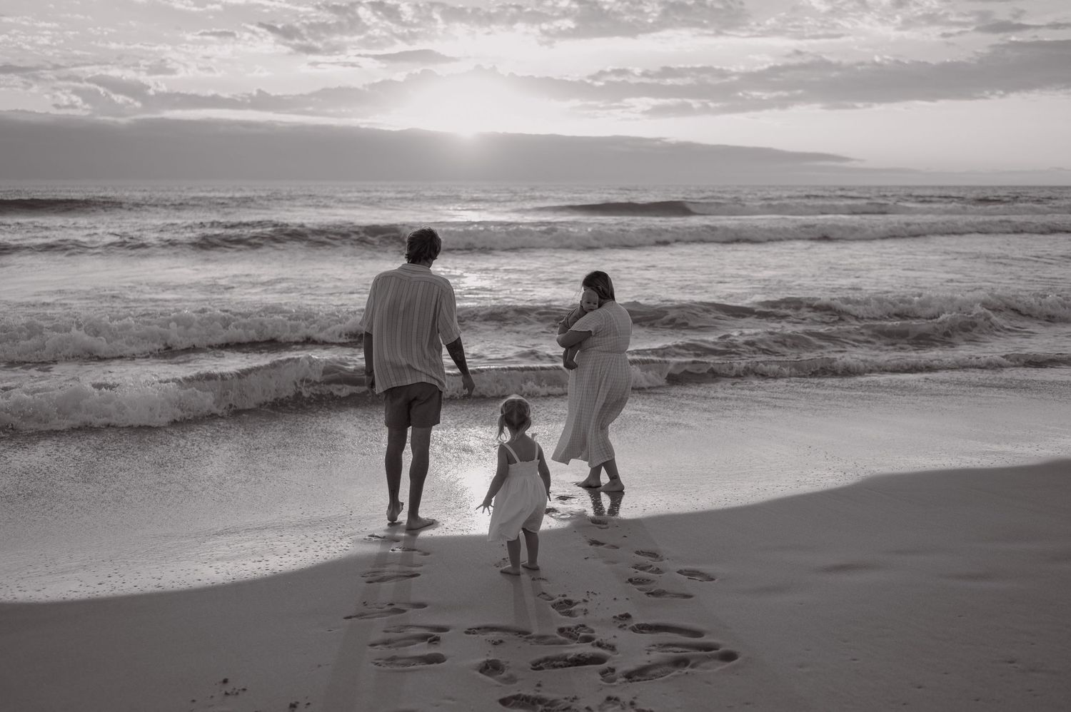 A family walks along a misty beach shoreline holding hands in black and white.