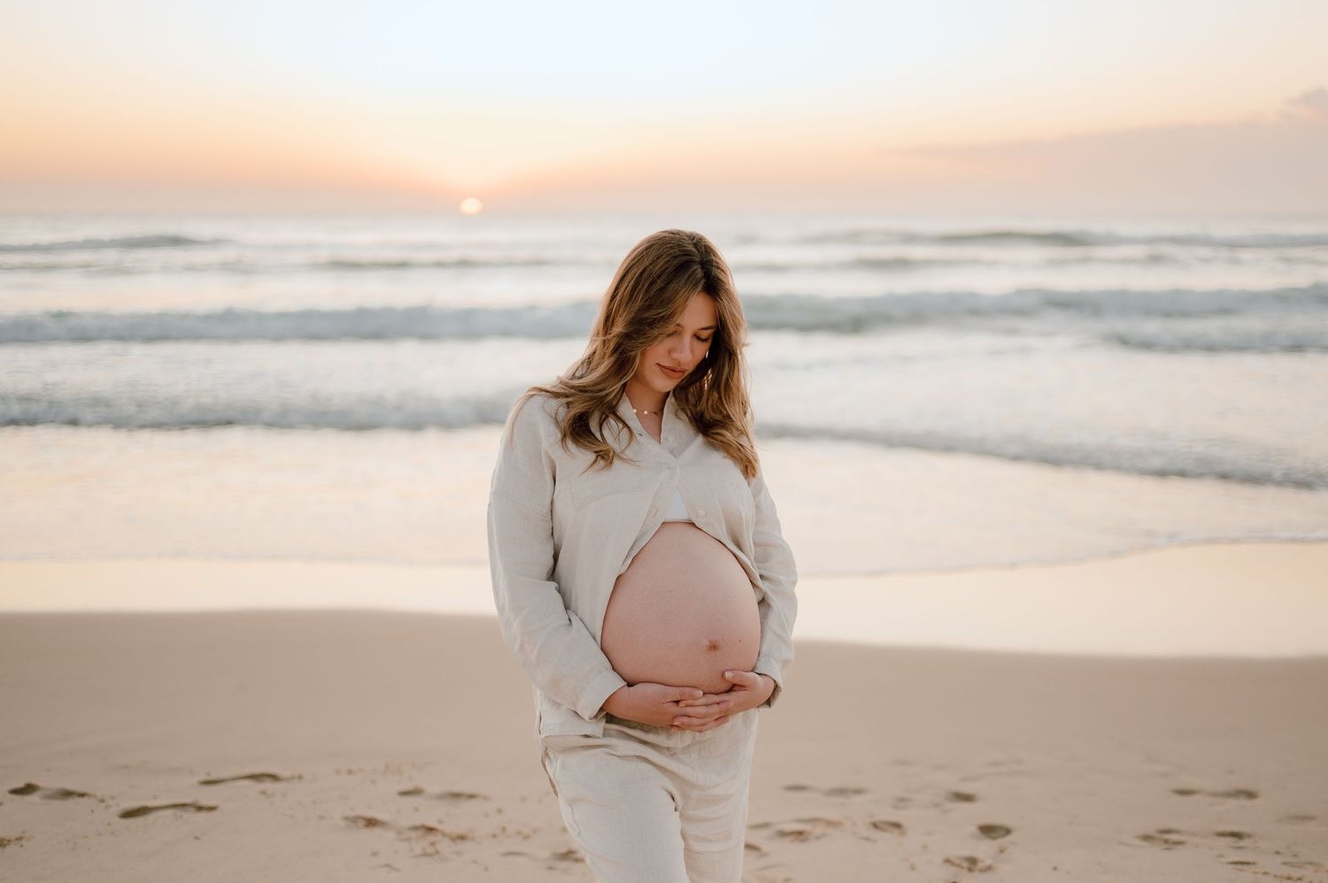 Maternity photoshoot at sunset on a peaceful beach with footprints in the sand.