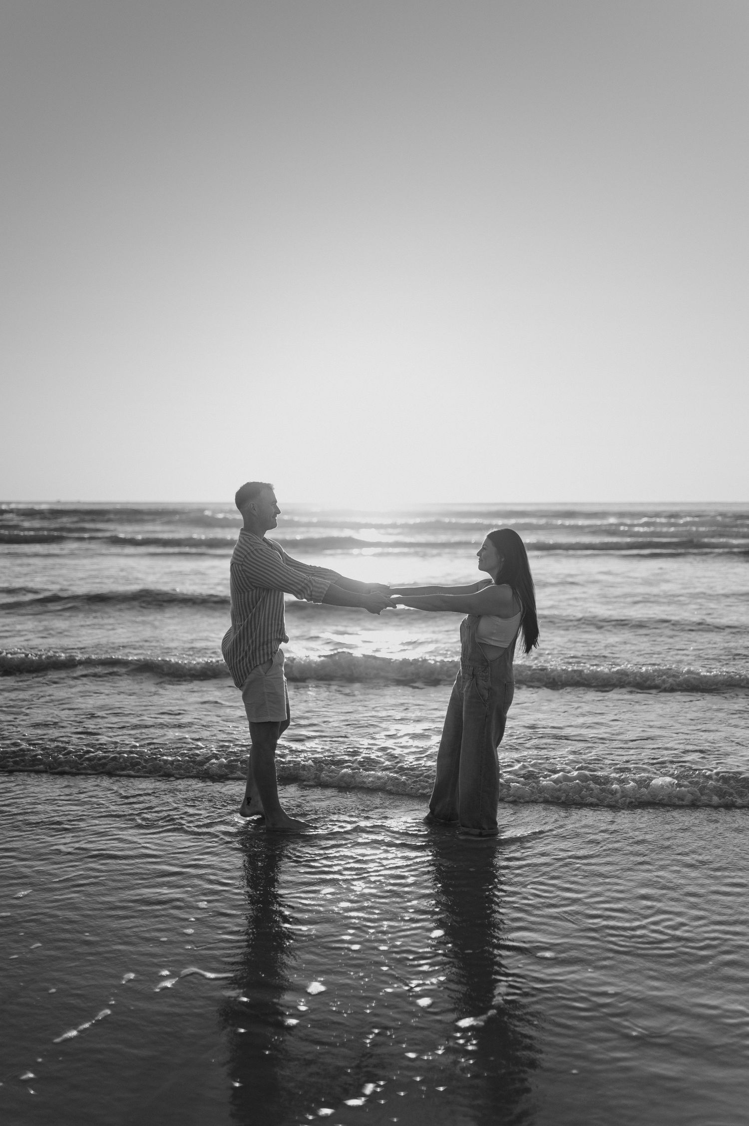 Silhouettes of figures standing in ocean waves at sunset.