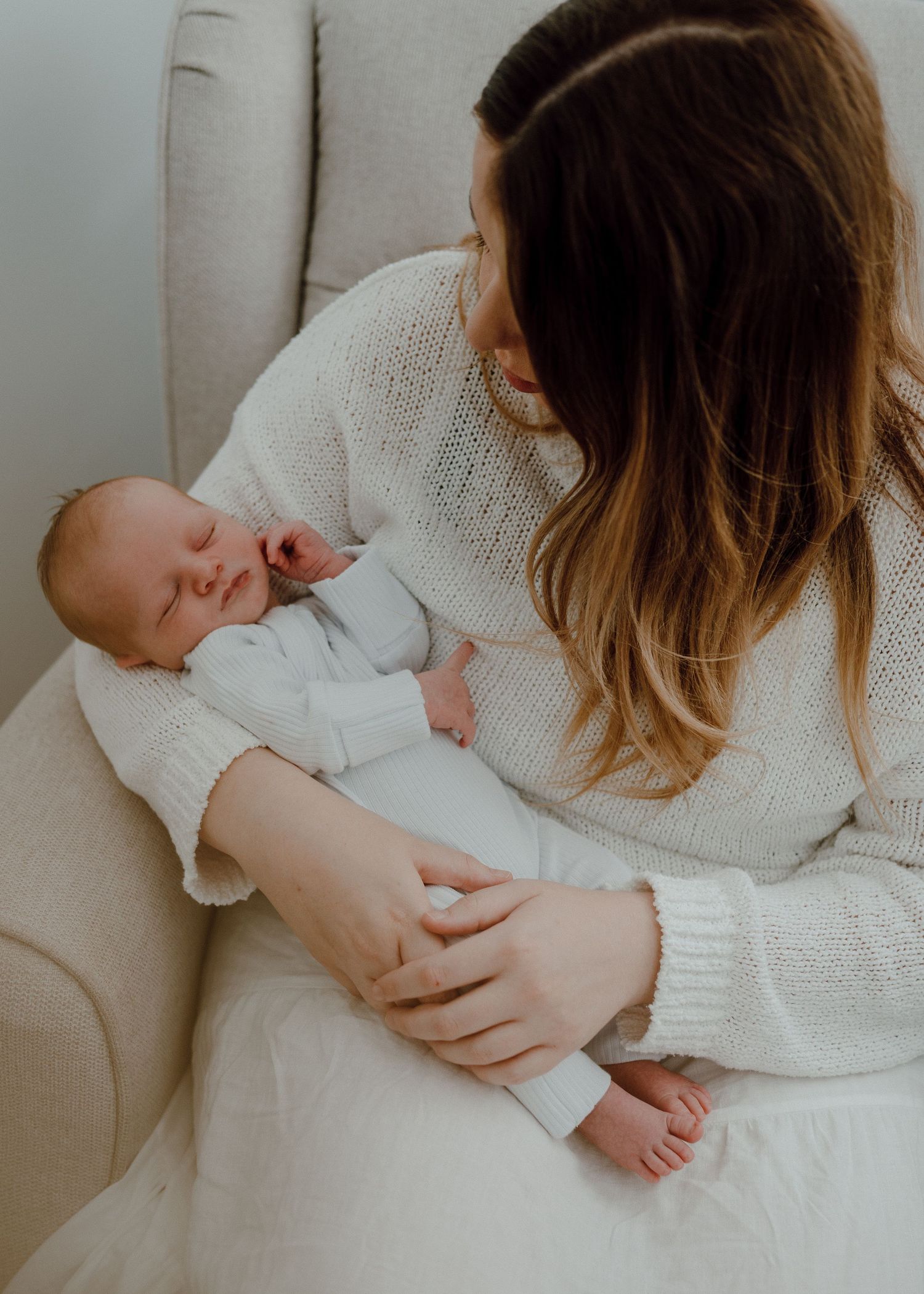 A tender series of photos showing a parent in white sweater embracing and snuggling with a sleeping newborn baby.