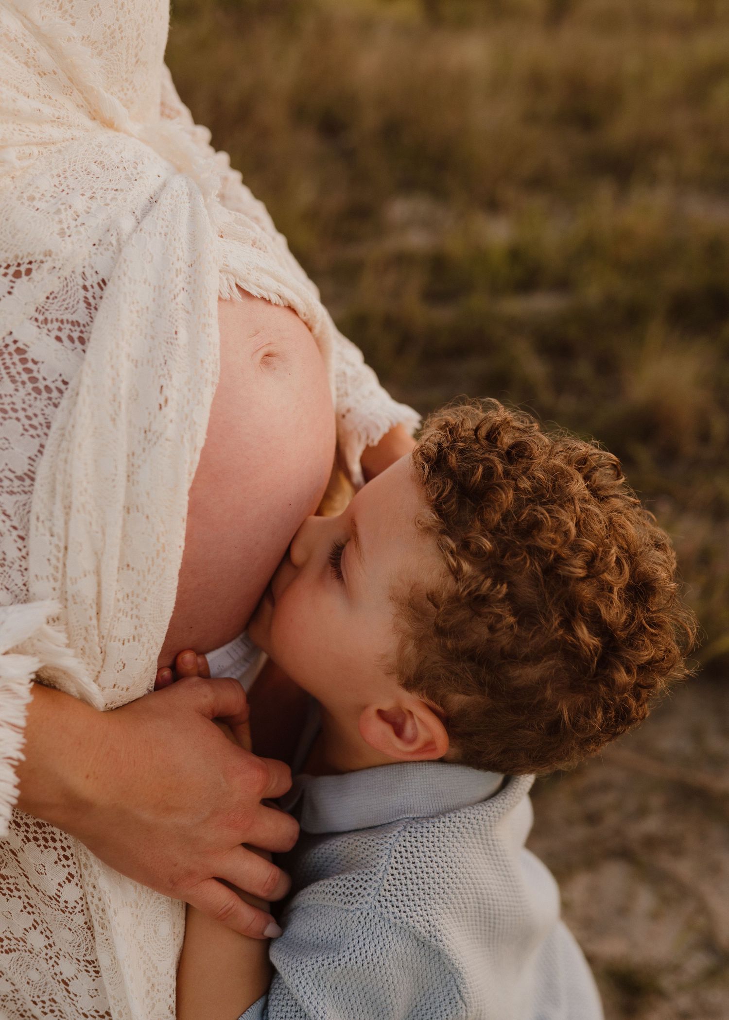 A romantic couple sharing an intimate kiss in white lace dress and casual attire during golden hour.