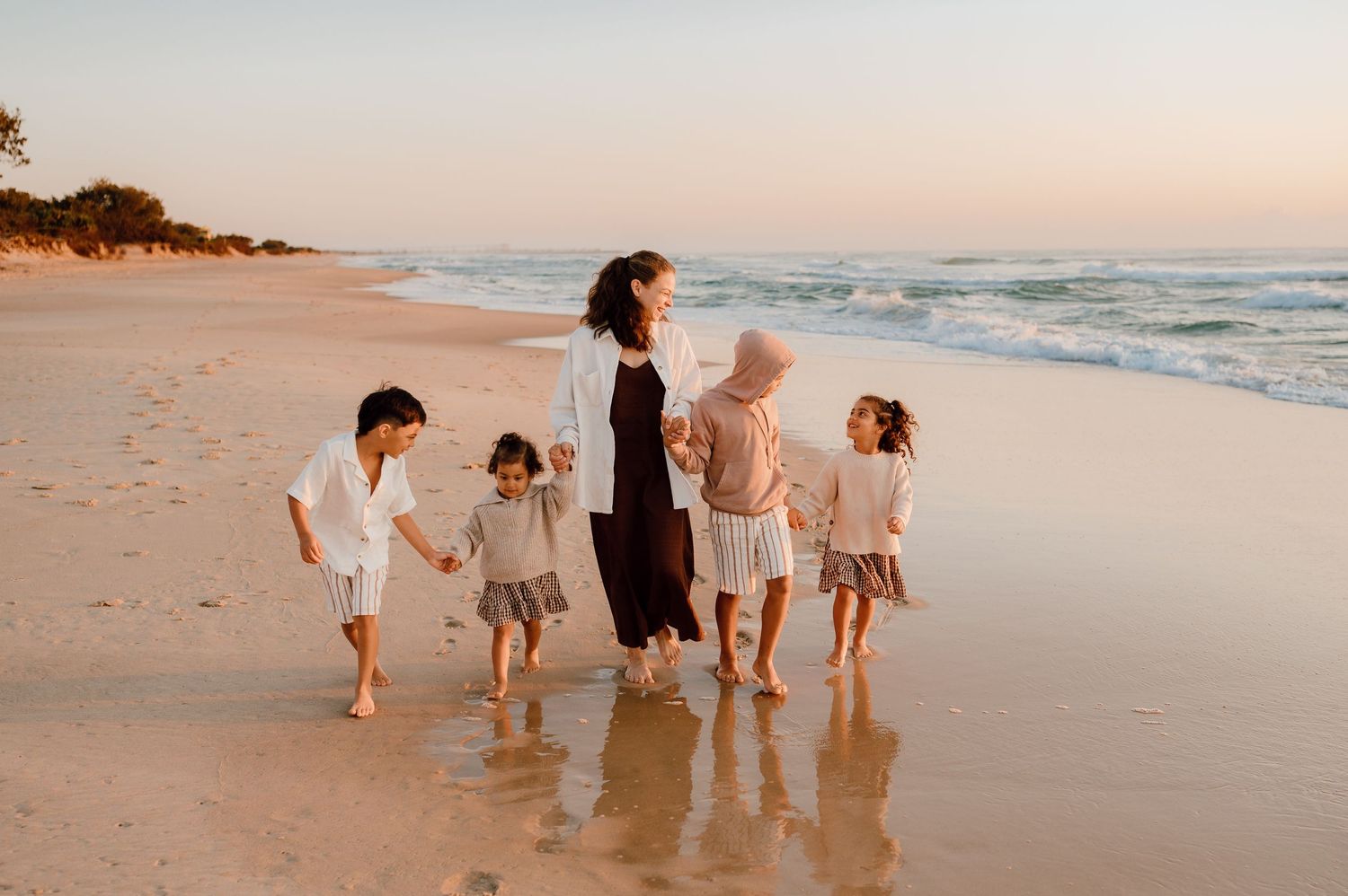 Group walking along shoreline during golden hour on sandy beach.