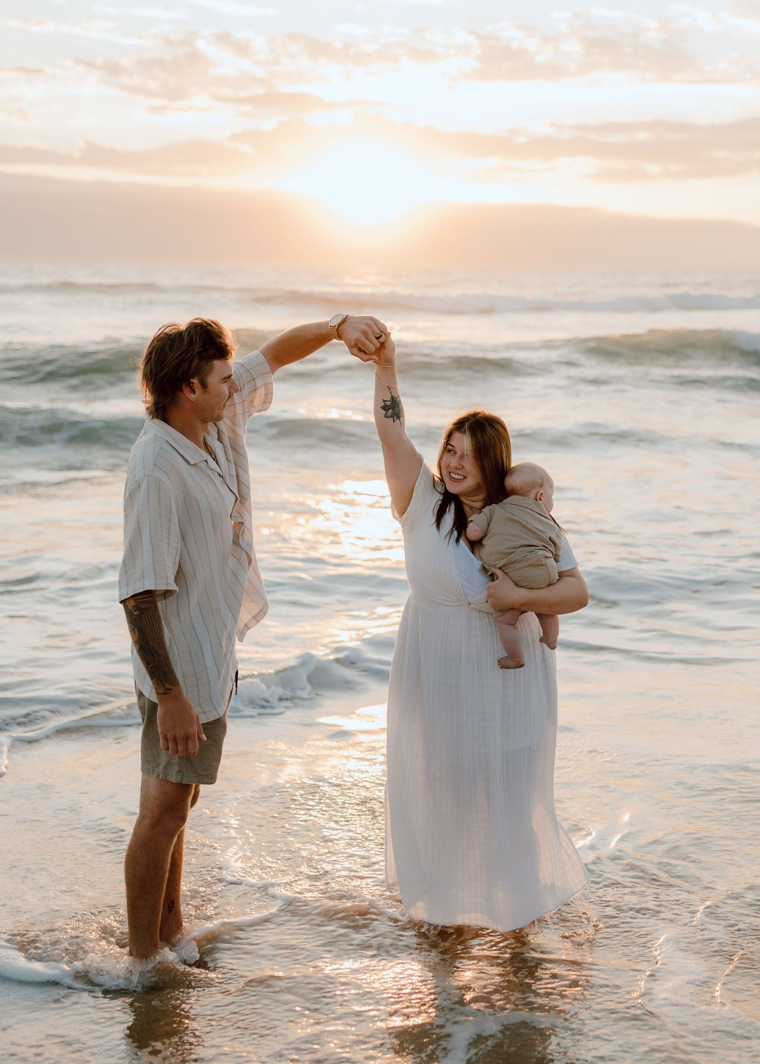 Family playing in ocean waves during golden hour sunset.