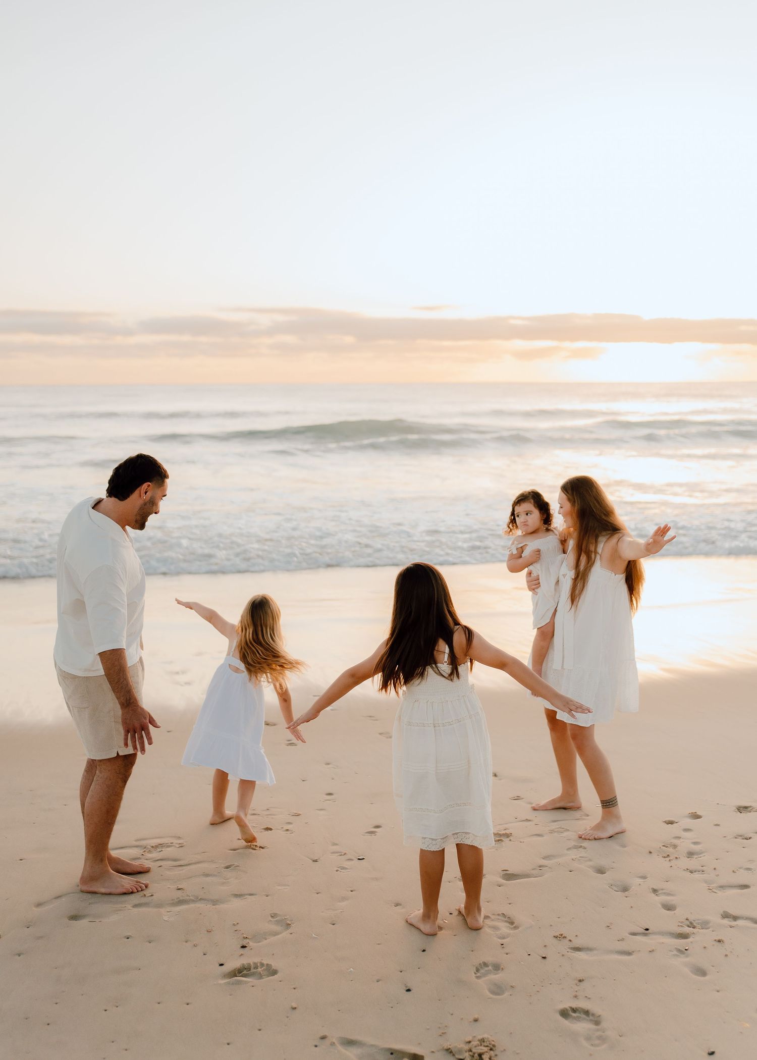Family playing together and holding hands while walking on a sandy beach at sunset.