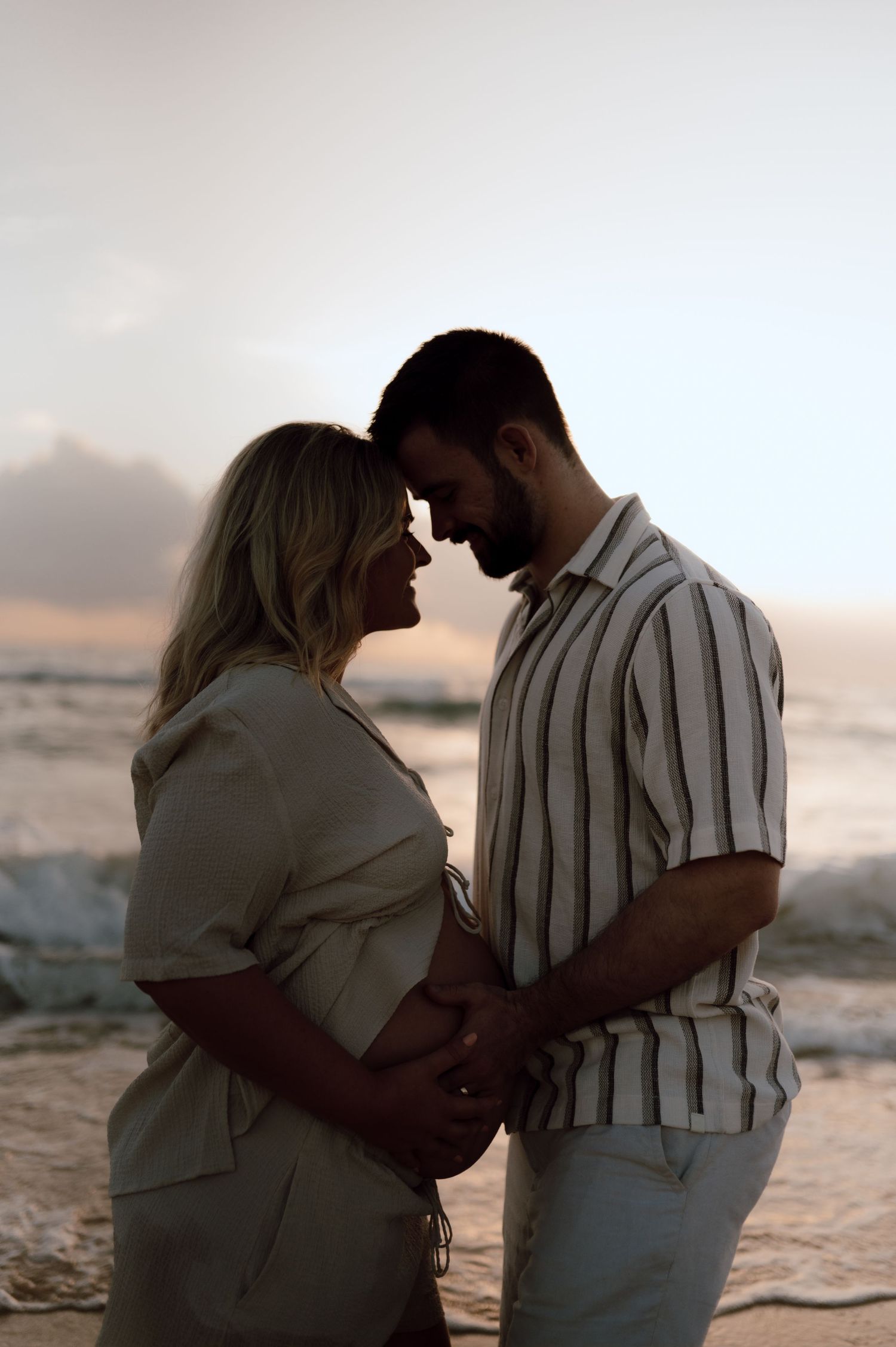 Silhouetted couple embraces on beach at sunset.