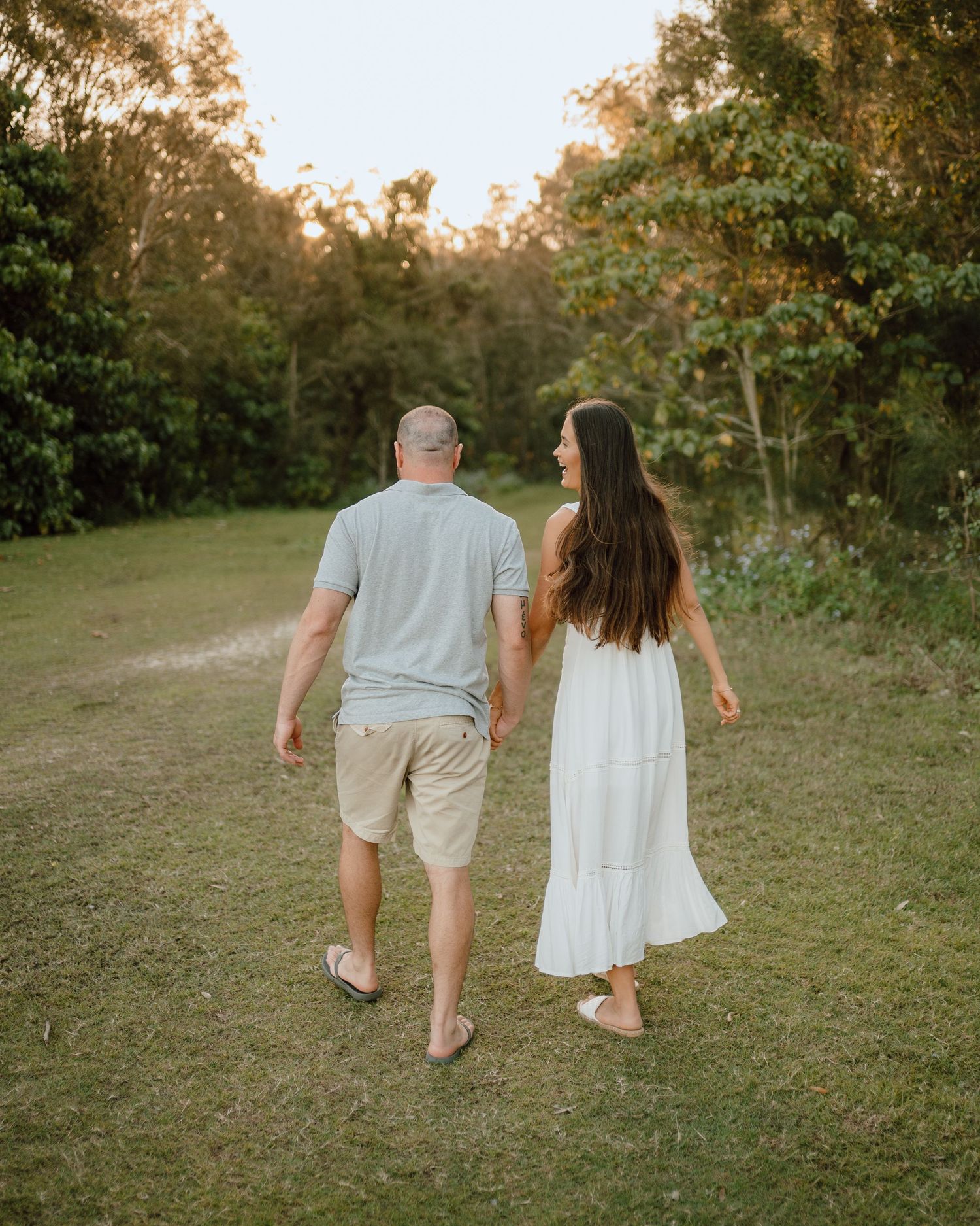 A couple walks together on a grassy path during golden hour.