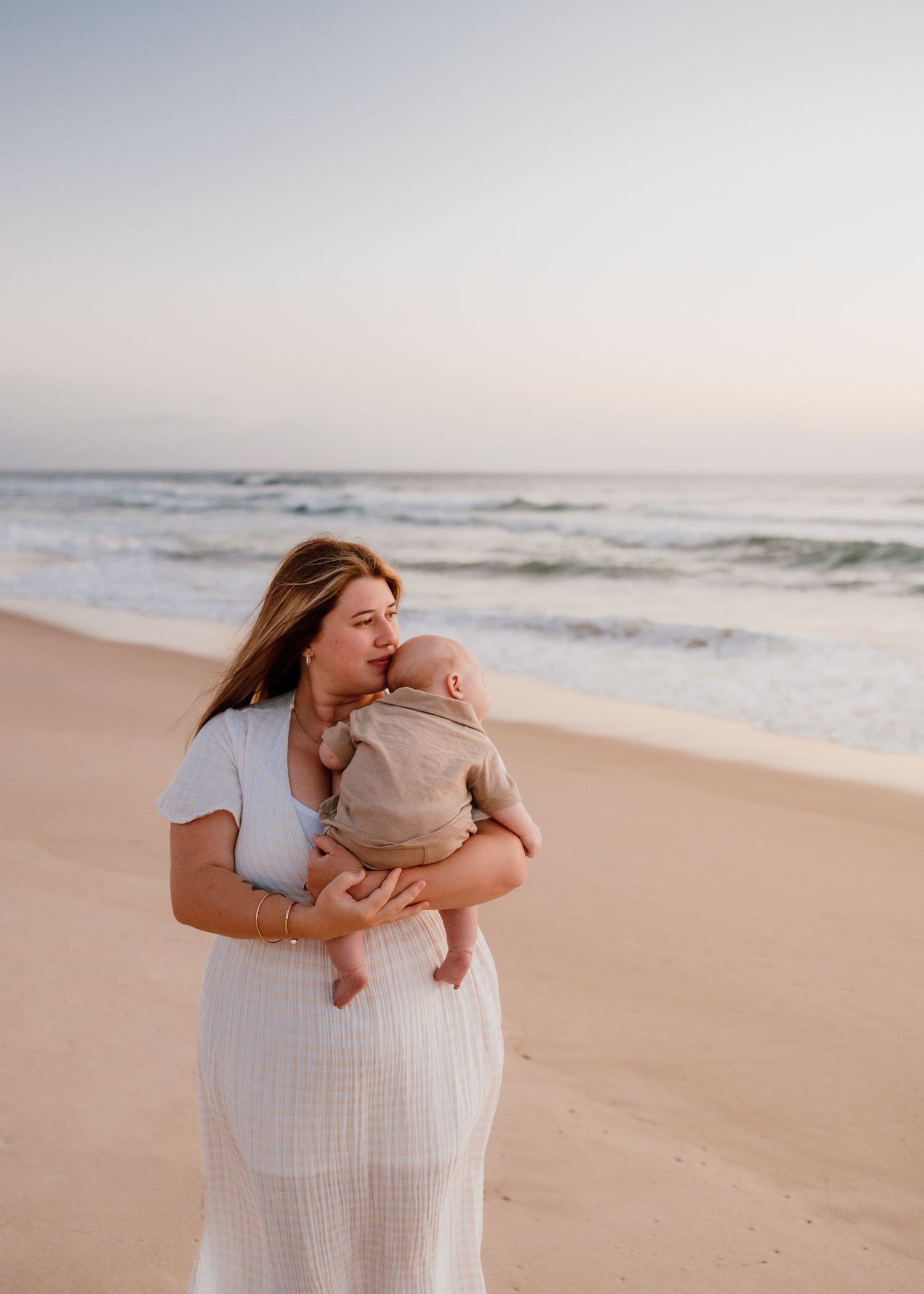 Mother and baby share intimate moments on a peaceful beach at sunset.