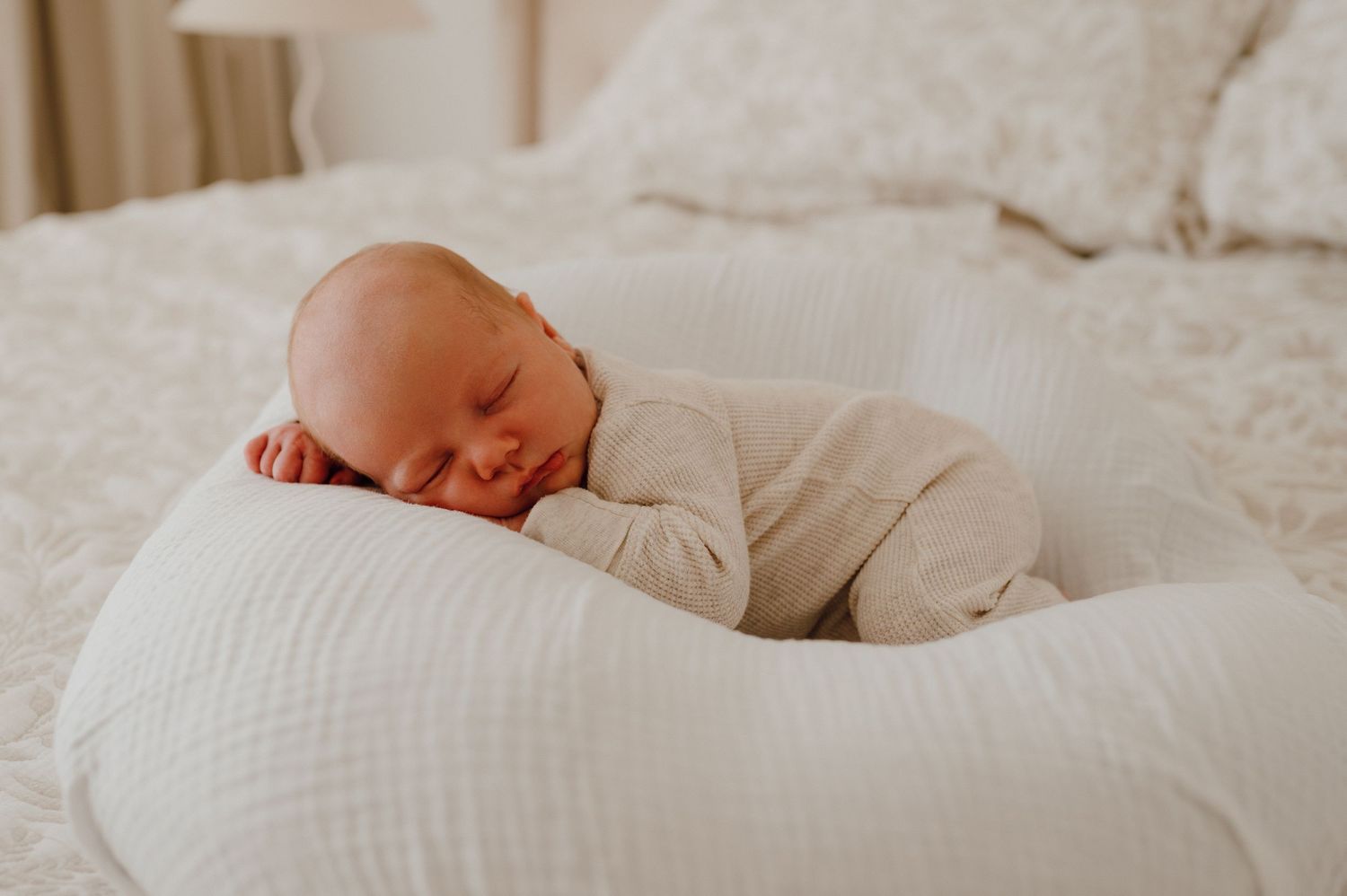 Newborn baby sleeping peacefully on a white nursing pillow on a soft bed.