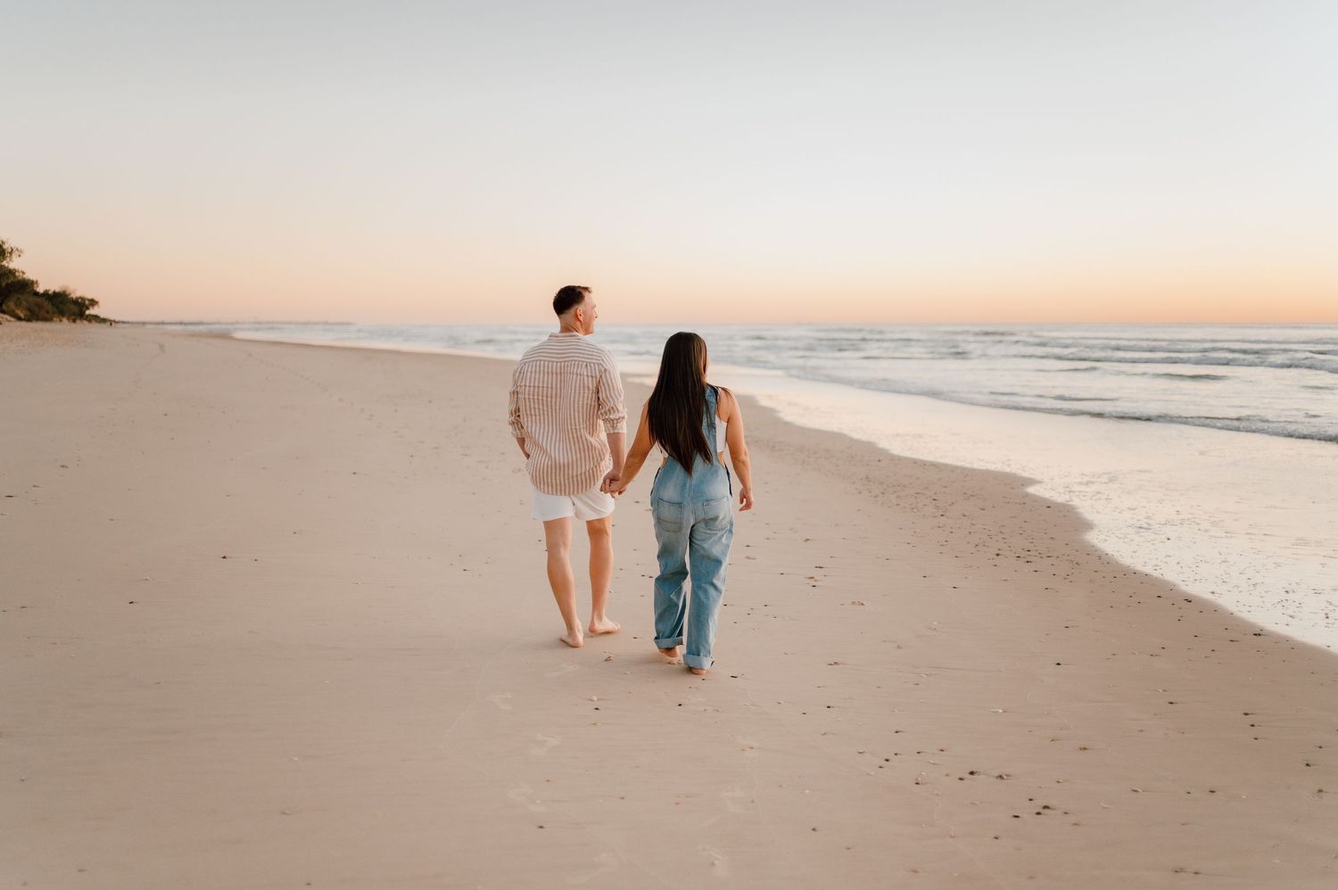 Couple walking along empty beach shoreline at sunset.