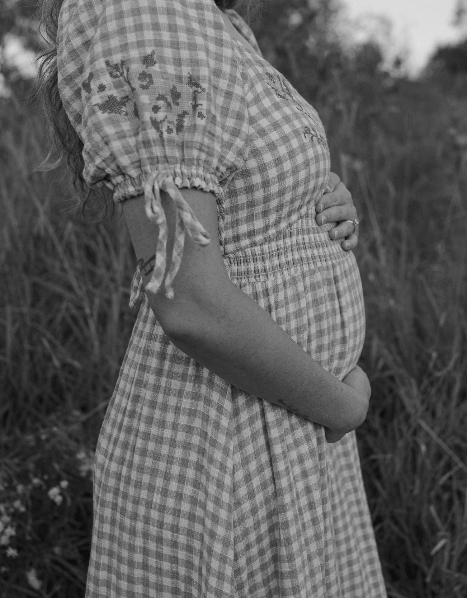 Black and white series showing the profile of a pregnant belly in a gingham dress.
