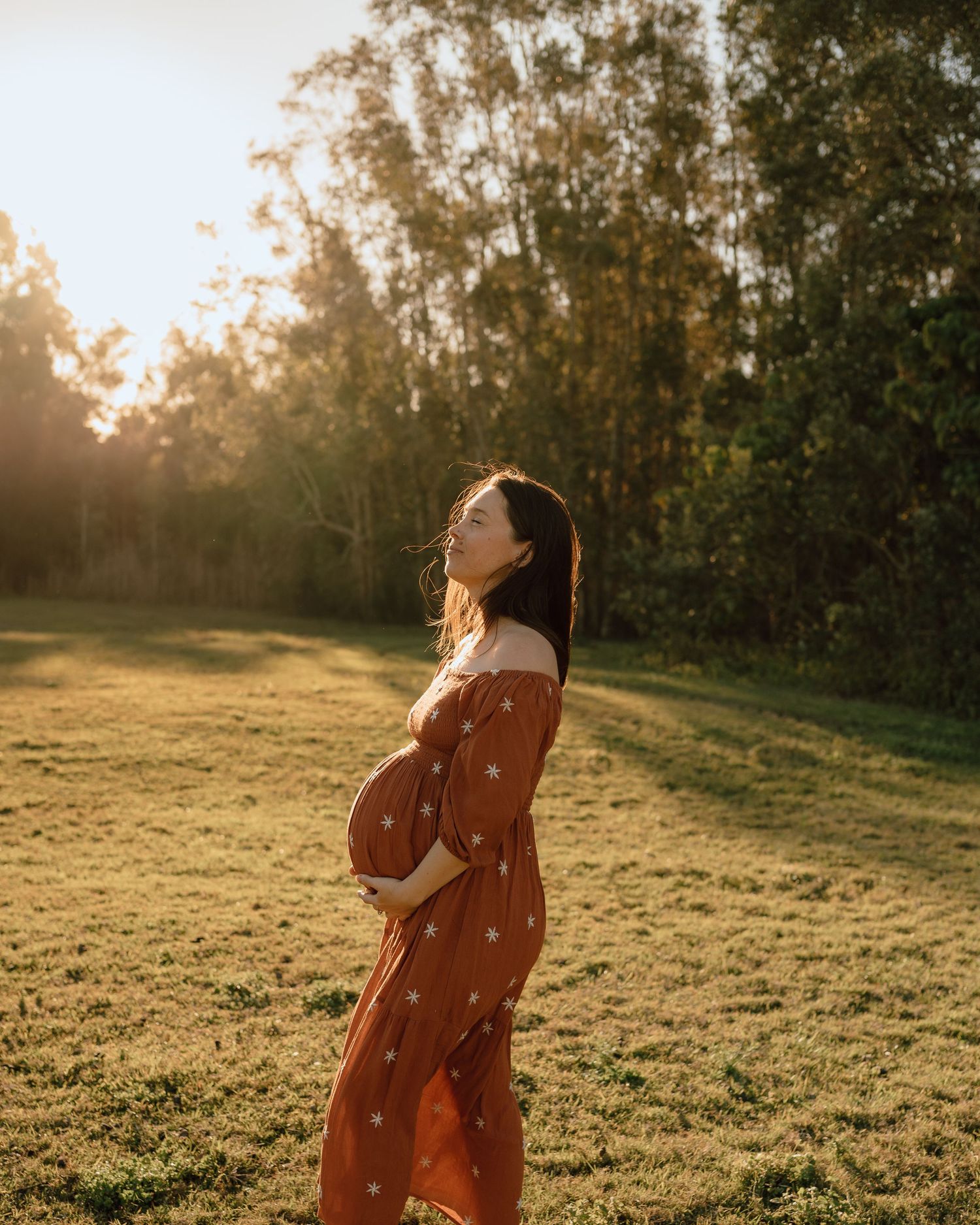 Woman in orange dress twirls playfully in a sunlit field at golden hour.