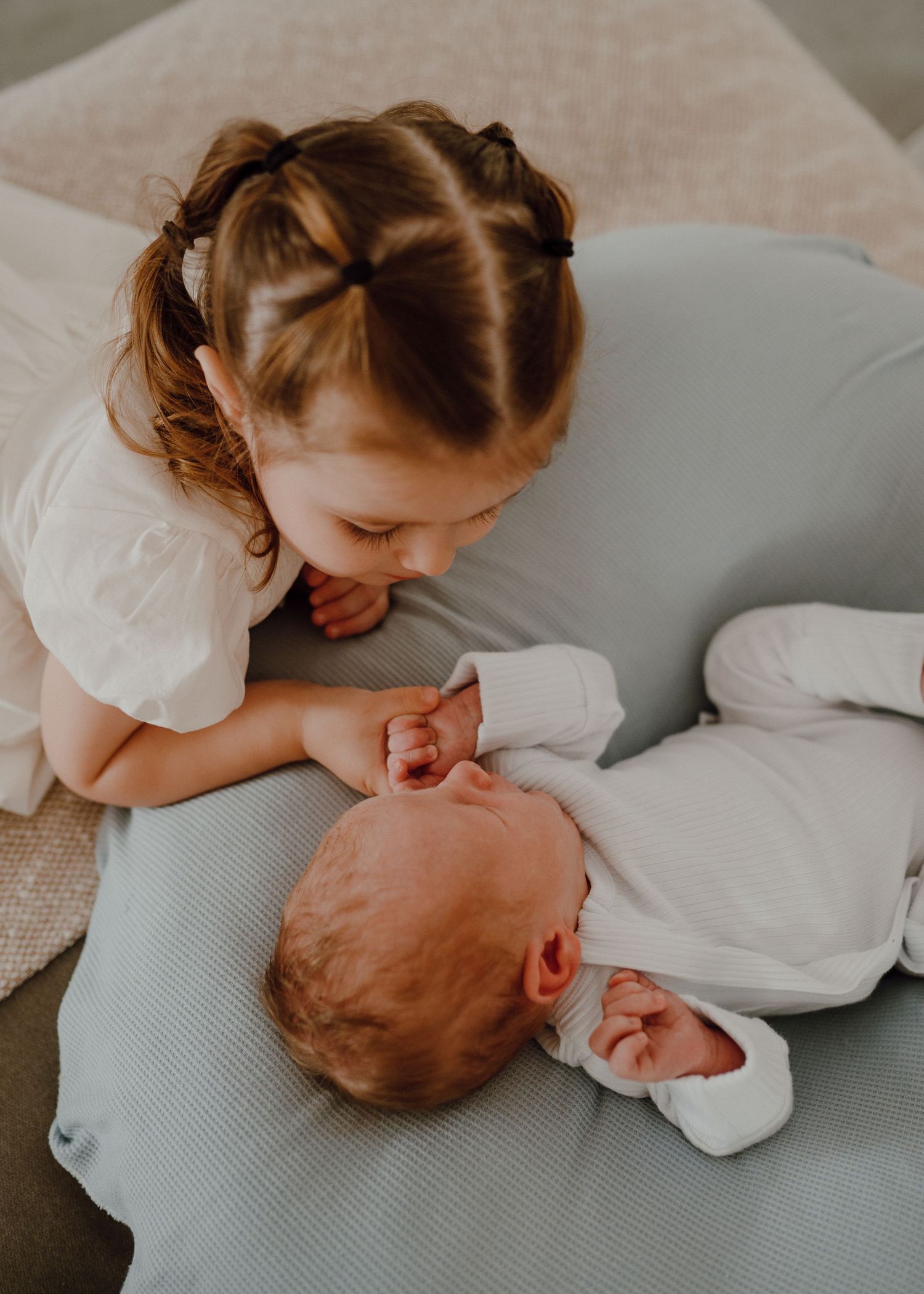 A sequence of sweet interactions between siblings as they share affectionate moments on a gray couch.