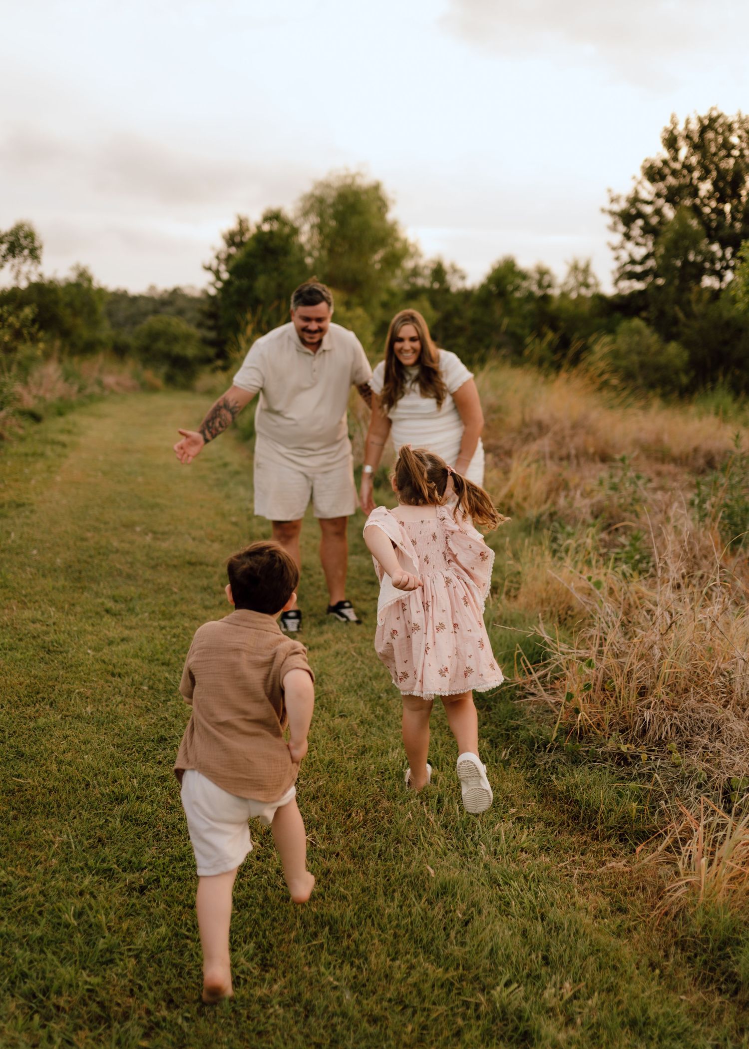 A couple in neutral tones and floral dress walk hand in hand through a grassy field at sunset.