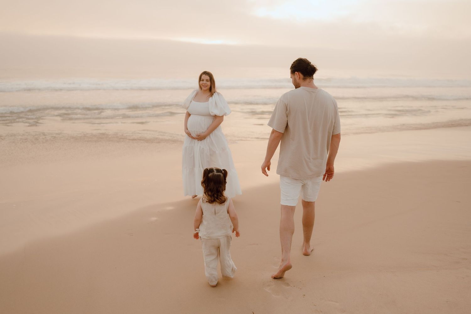 A family walks together on a serene beach at sunset, with soft waves rolling in the background.