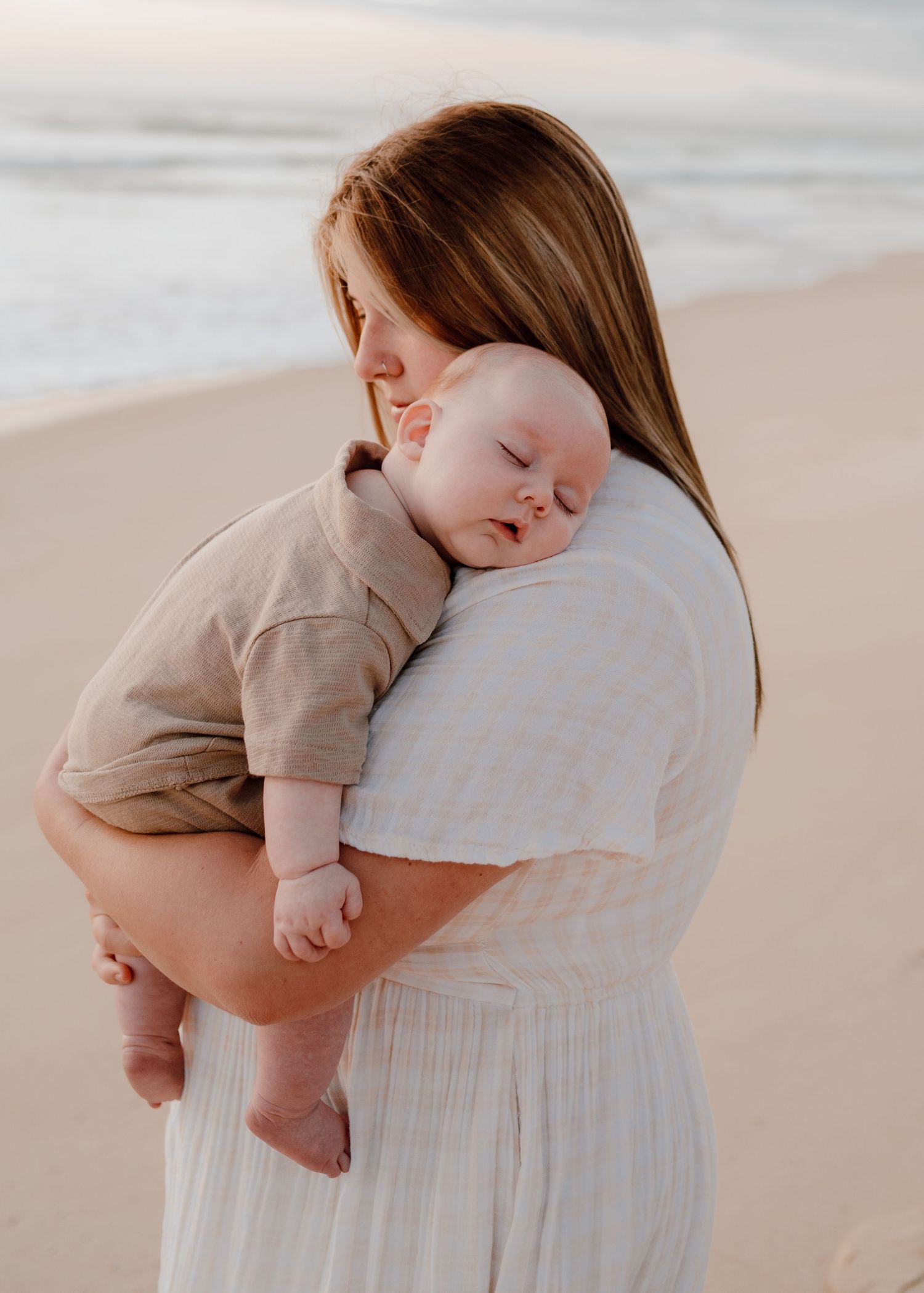 Tender moment captured between parent and baby against a beach backdrop.