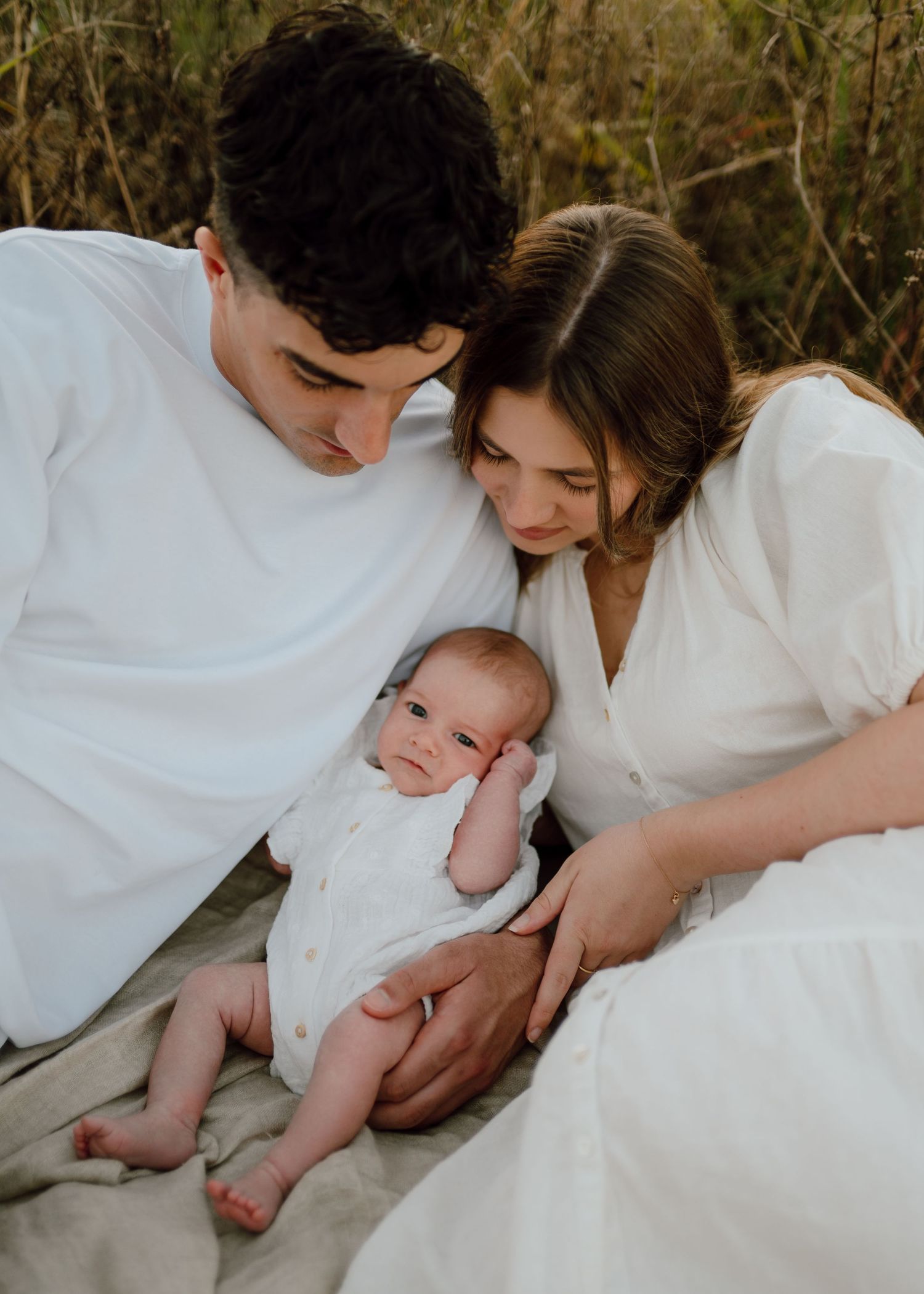 A tender family moment captured on a white blanket outdoors.