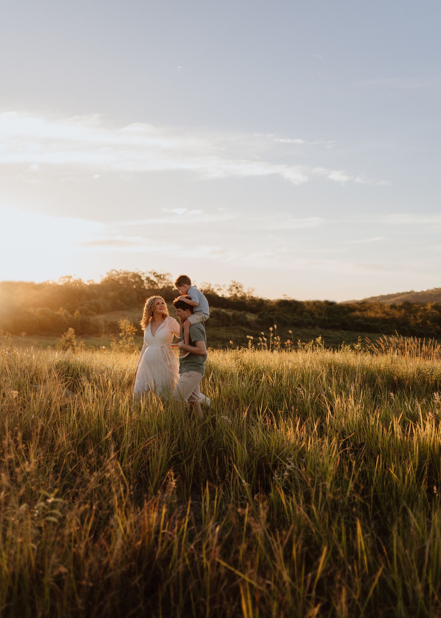 A couple embraces in a golden field at sunset with mountains in the background creating a romantic silhouette.