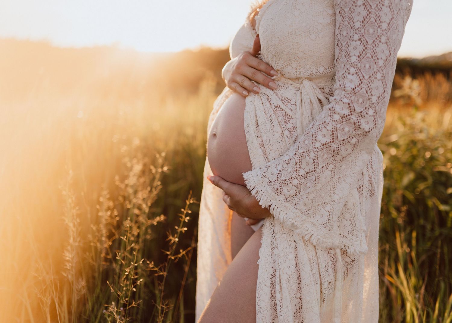 Silhouetted maternity photo in white lace dress during golden hour sunset in a wildflower field.