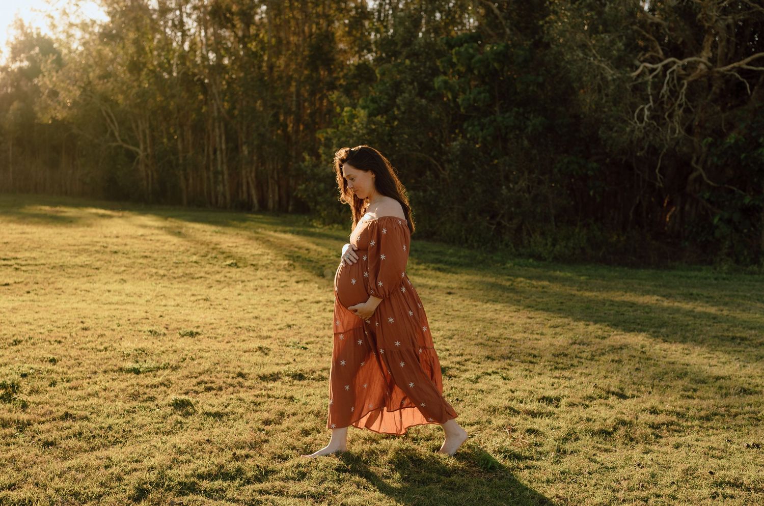Woman in a flowing red dress walking through a sunlit meadow at golden hour.