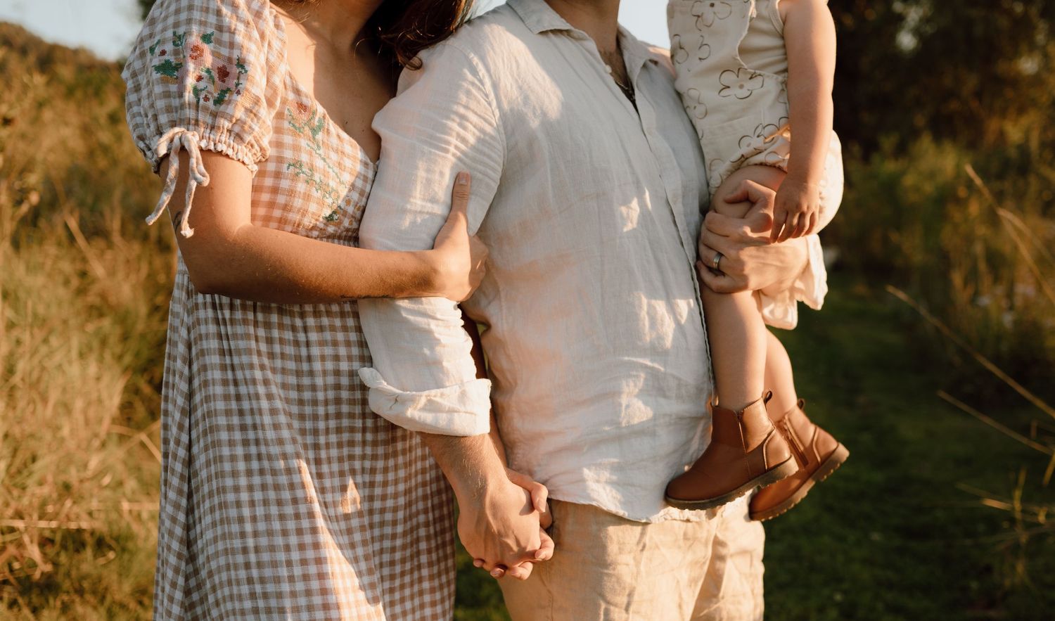 Family holding hands together in warm sunset light outdoors.