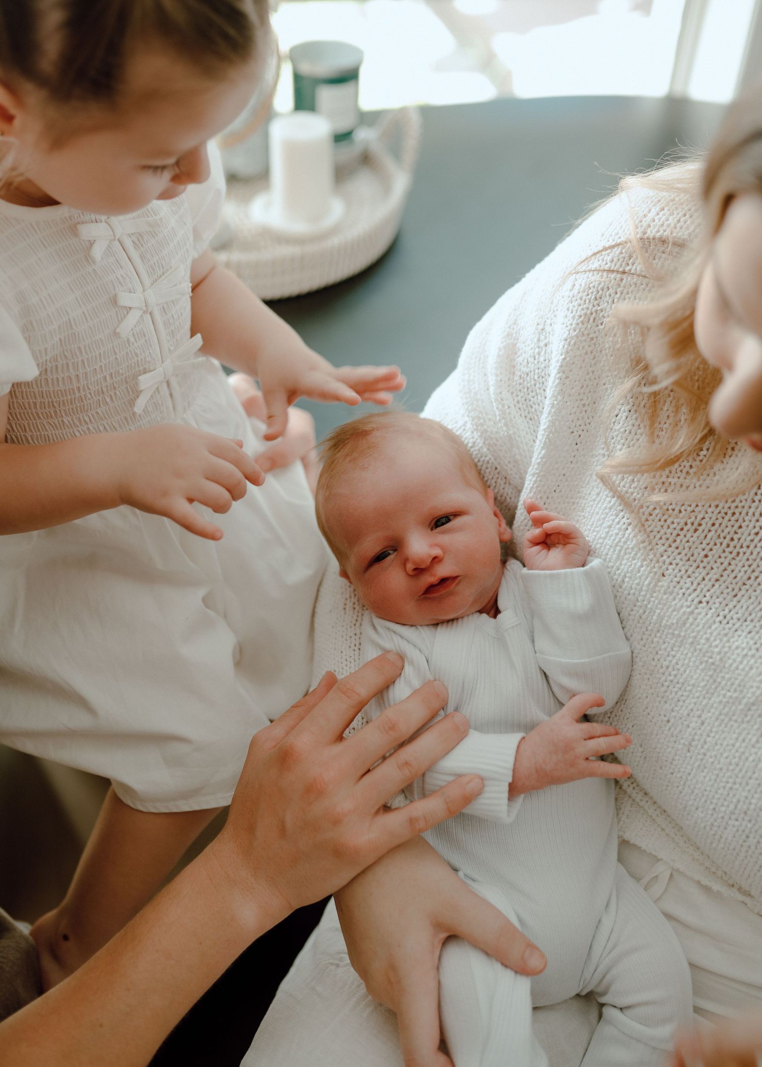 A series of tender moments showing hands gently caring for a baby wearing white clothing in soft natural light.