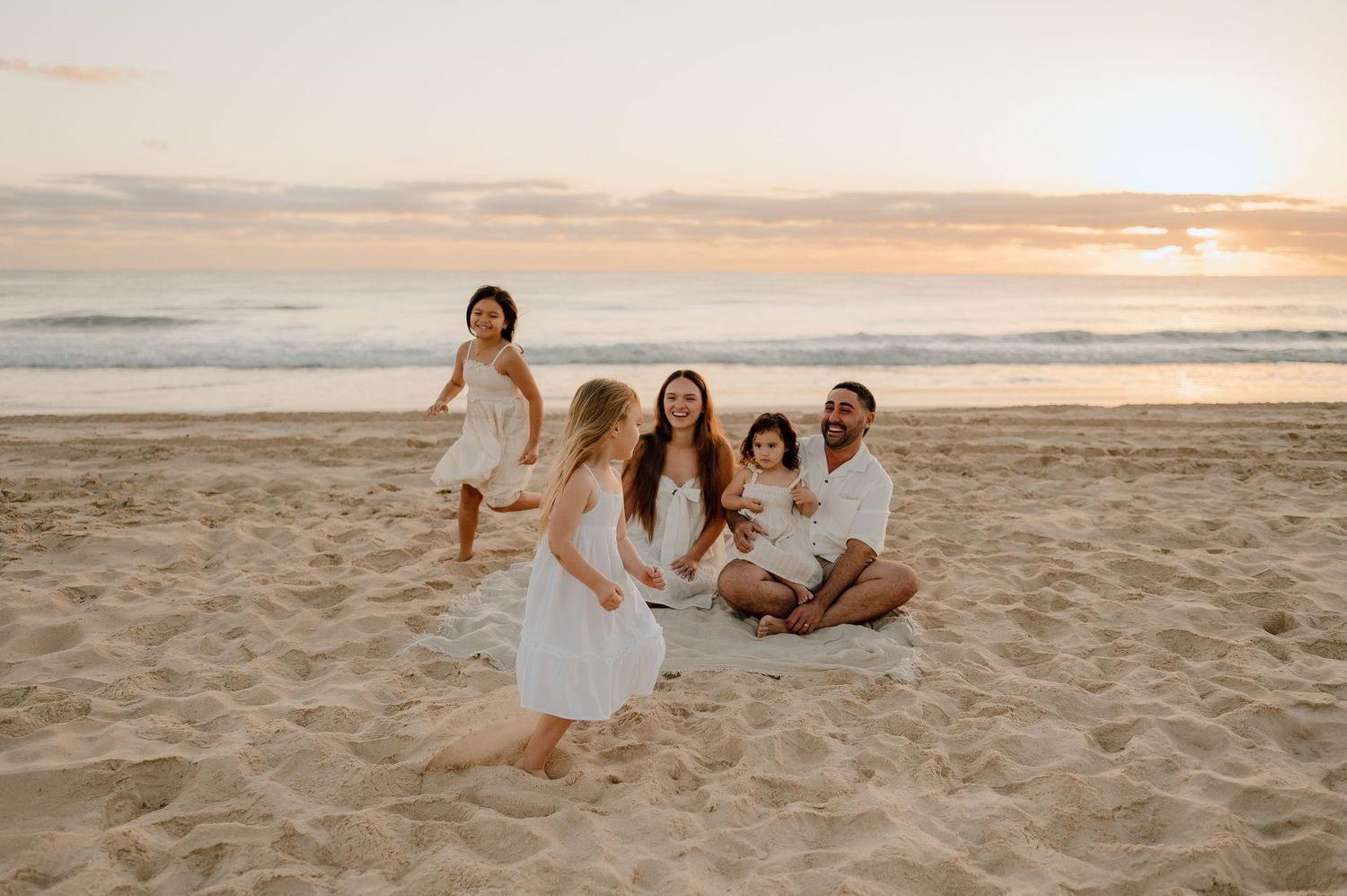 A group enjoys a relaxing evening together on a sandy beach at sunset with golden light illuminating the scene.