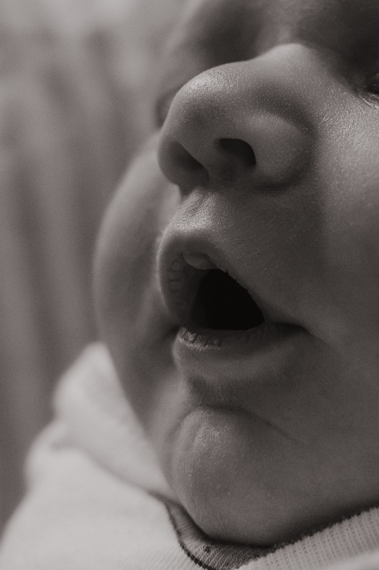 Close-up black and white photo of a newborn baby's nose and open mouth, showing delicate infant features.