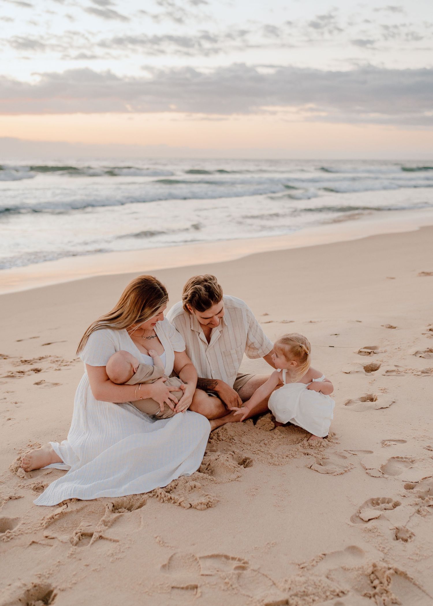 A family sits together on a beach at sunset with waves rolling in the background.