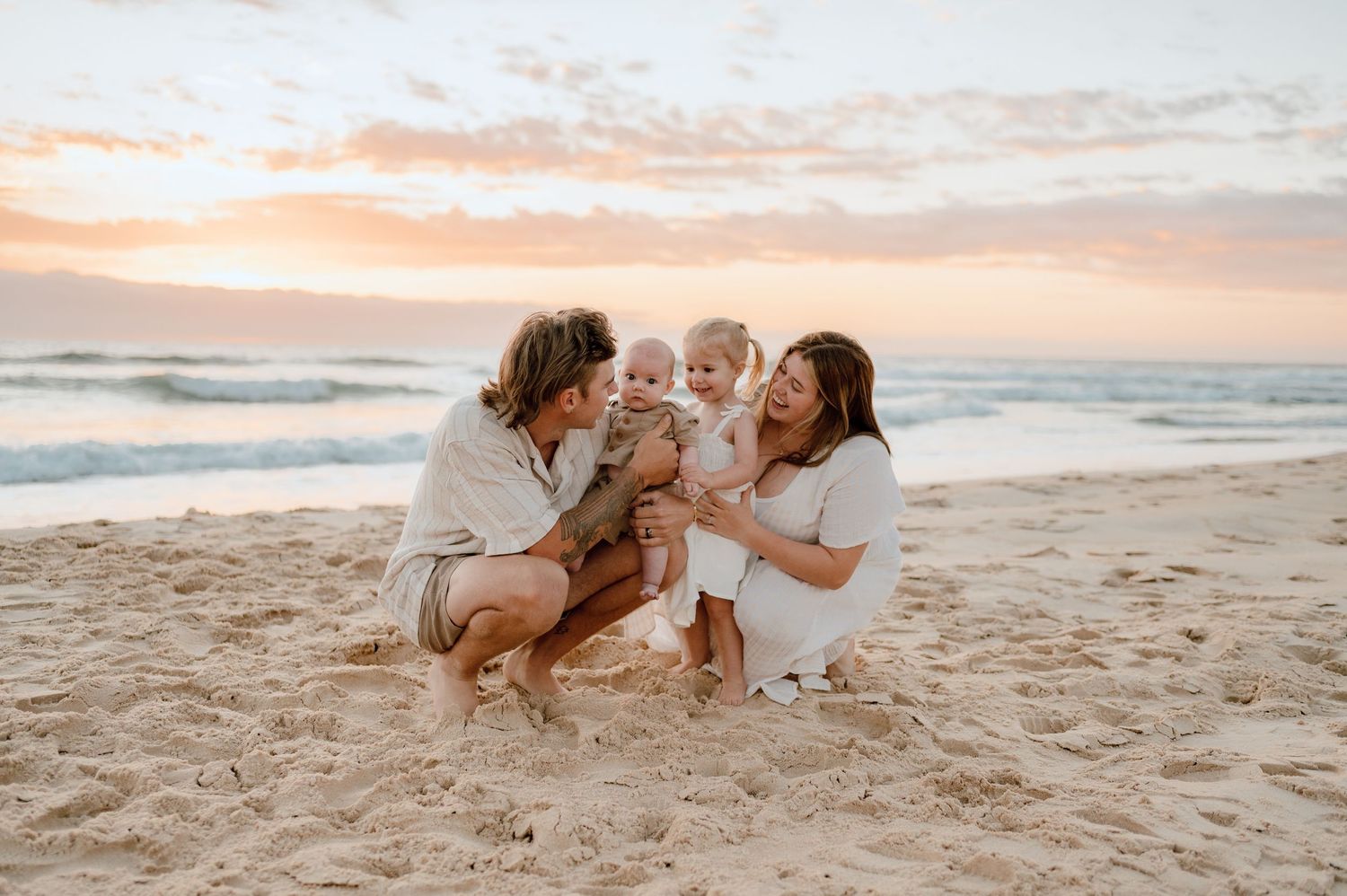 A family shares a playful moment together on a sandy beach at sunset.