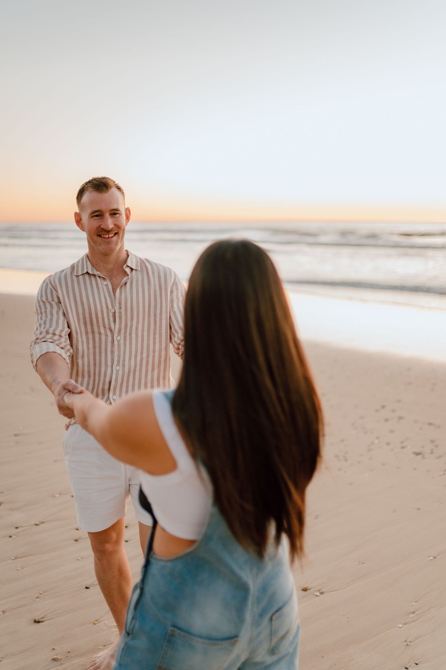 Couple laughing and dancing together on beach at golden hour.