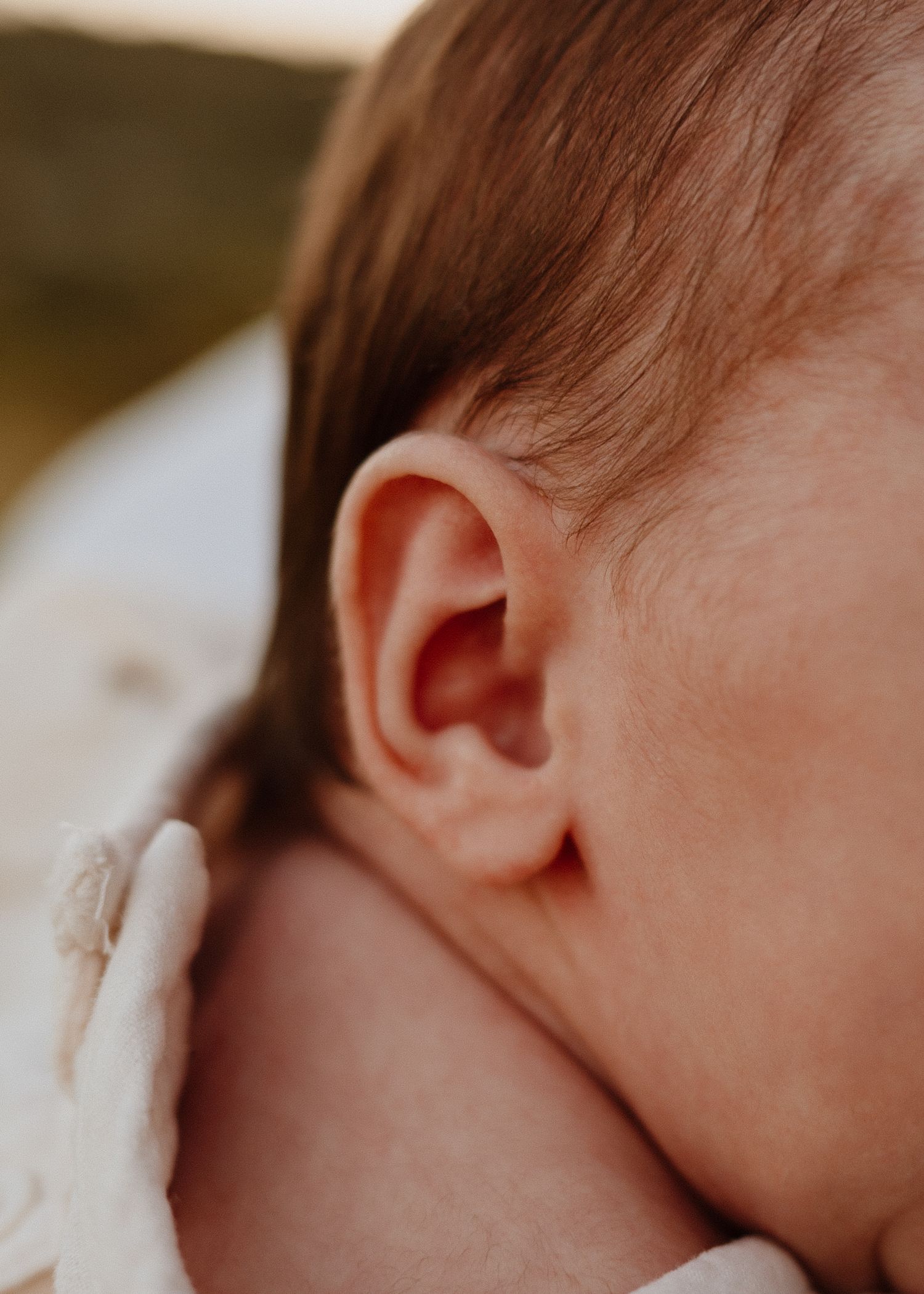 Close-up of a newborn baby's ear and delicate skin, captured in soft natural light during a newborn photography session.