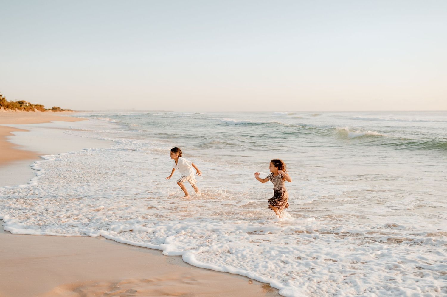 Two children playing in the ocean waves at sunset on a sandy beach.