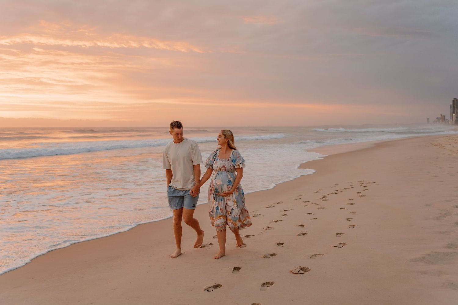 Footprints trail along a sandy beach at sunset as people walk together by the ocean shore.