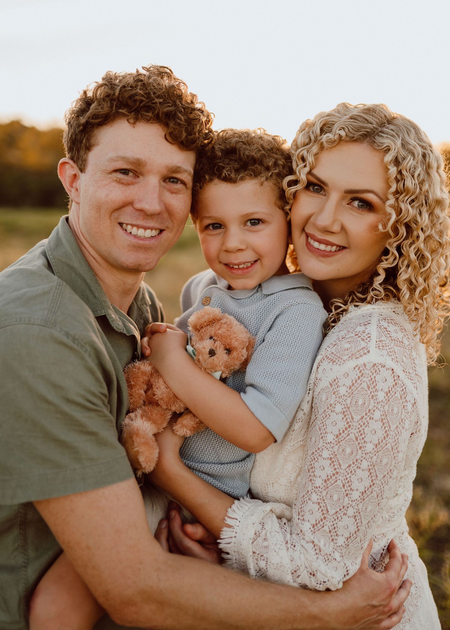 A happy family embraces while holding a small ginger kitten during a golden hour outdoor photoshoot.