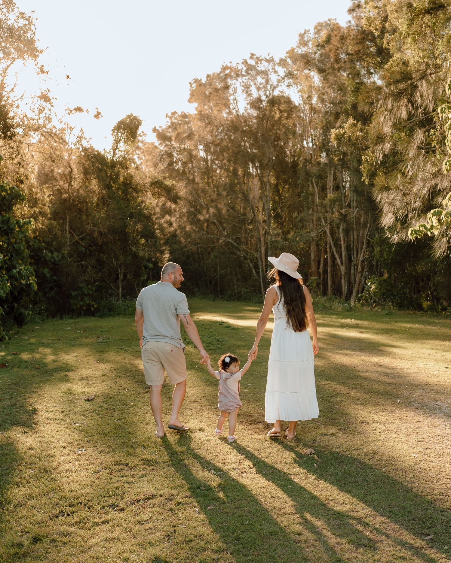 Family walks hand in hand through a grassy field with long shadows at sunset.