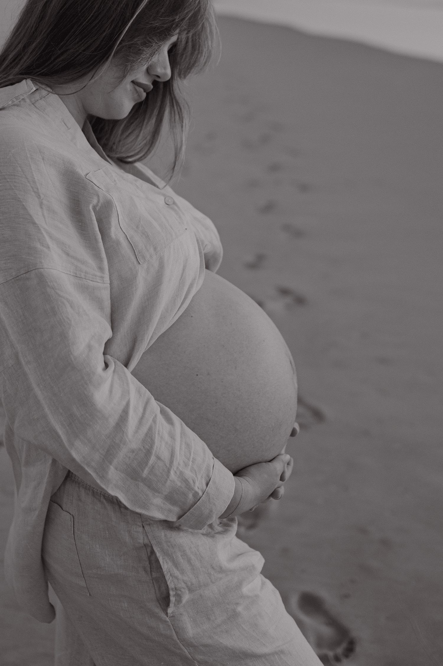 Intimate black and white maternity photography highlighting the baby bump on a beach.
