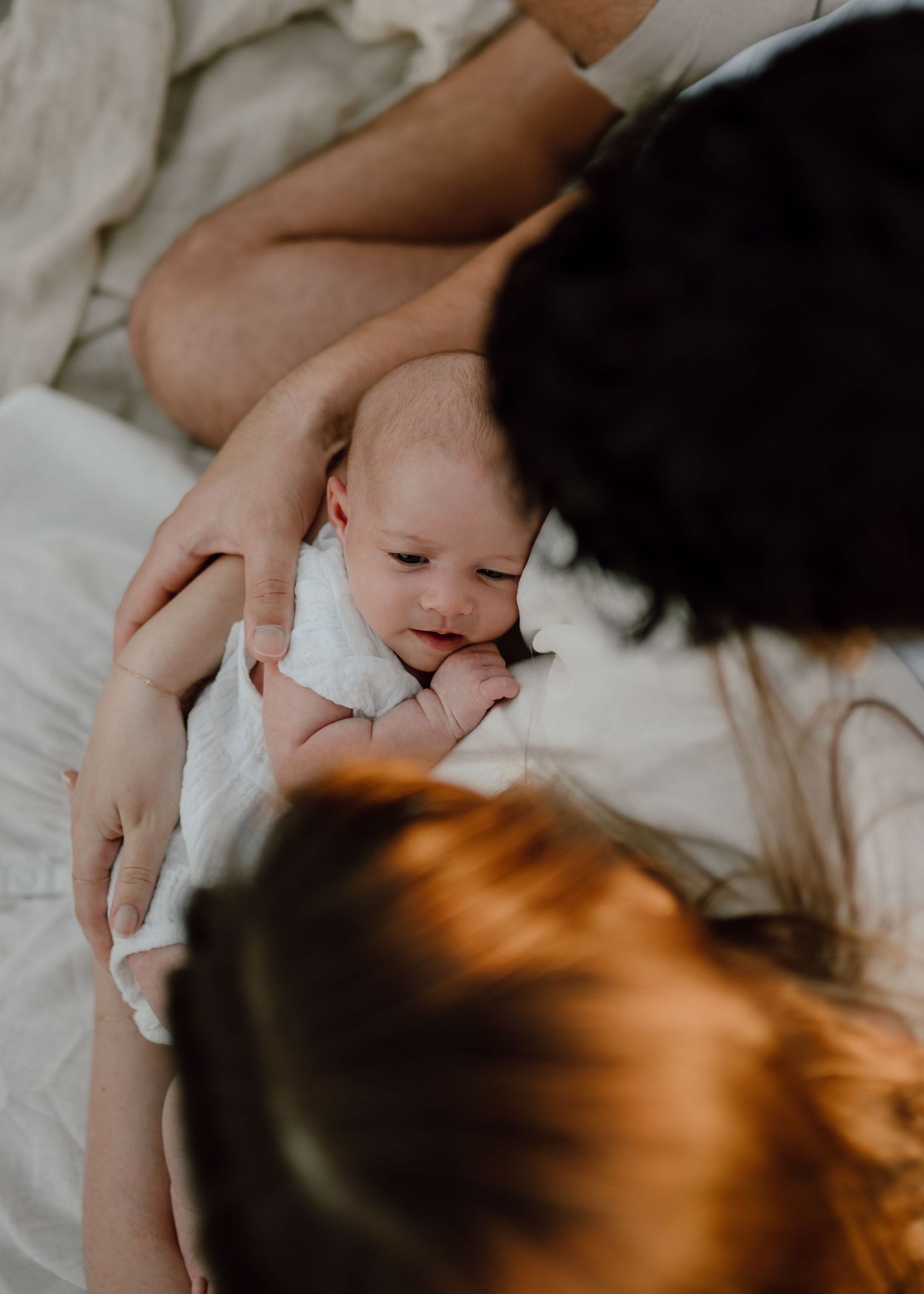 A tender moment captured in soft lighting as a baby lies on white bedding.